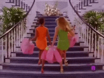 People in colorful dresses walking up a staircase with plants on either side.