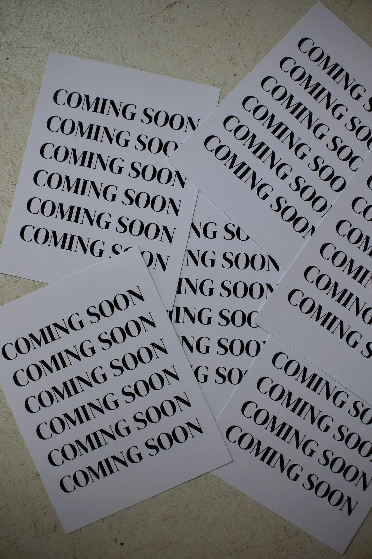 Multiple sheets of paper on a surface, each with the words "COMING SOON" written in large black letters.