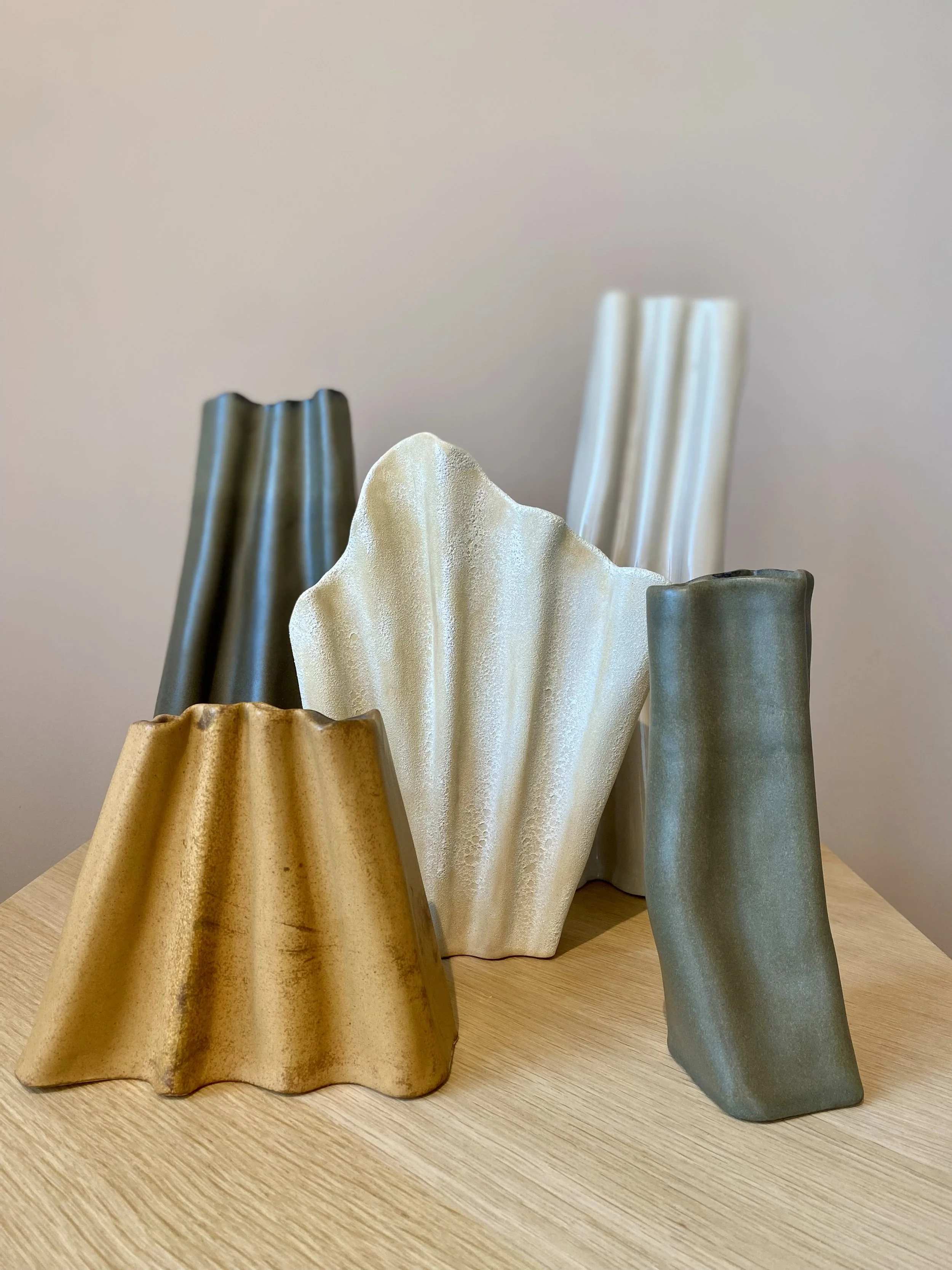 Four ceramic vases with varying heights and colors on a wooden surface with a plain background.