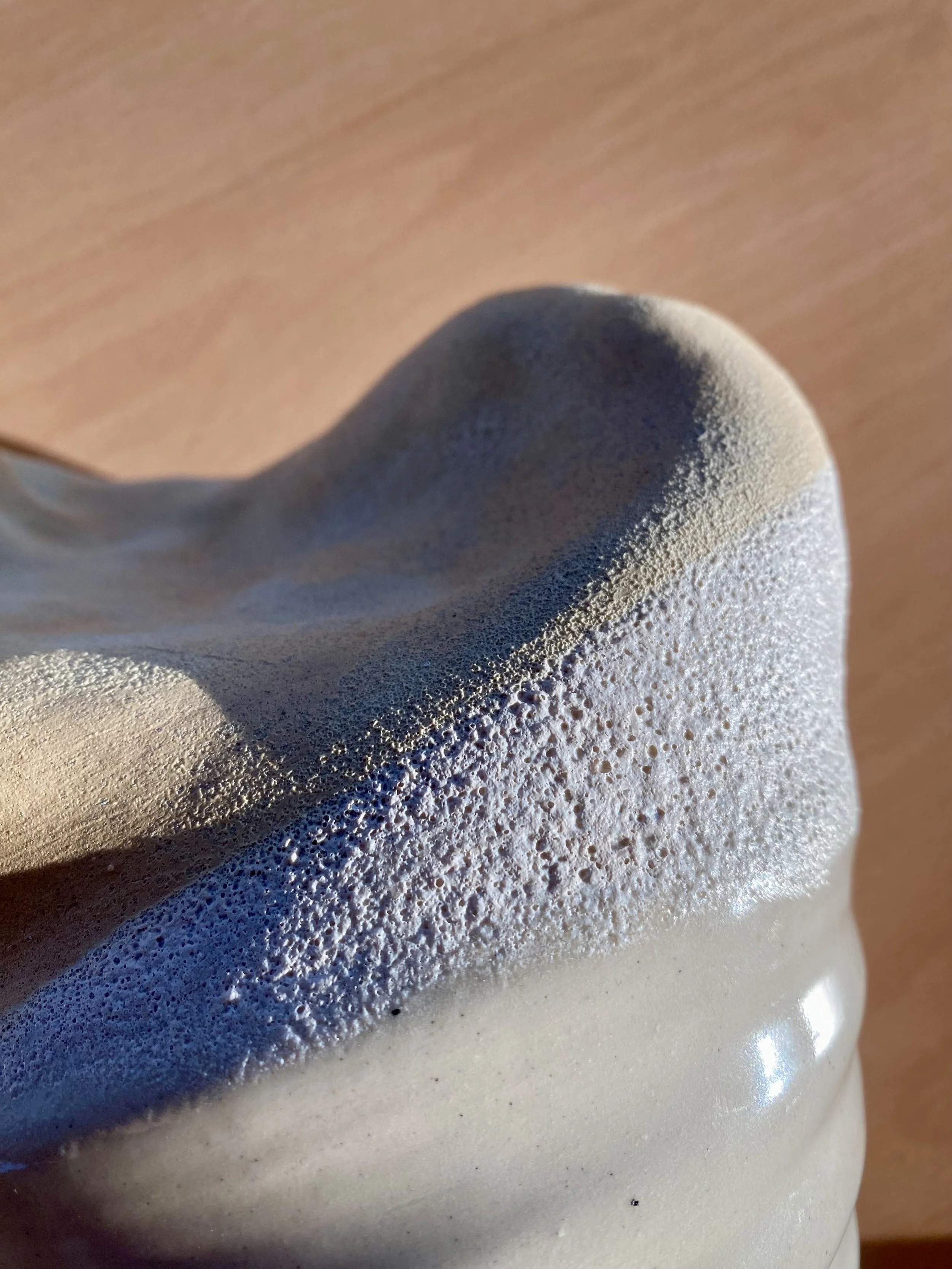 Close-up of a foamy, textured soap or shampoo lather on a surface, with light casting shadows on the foam.