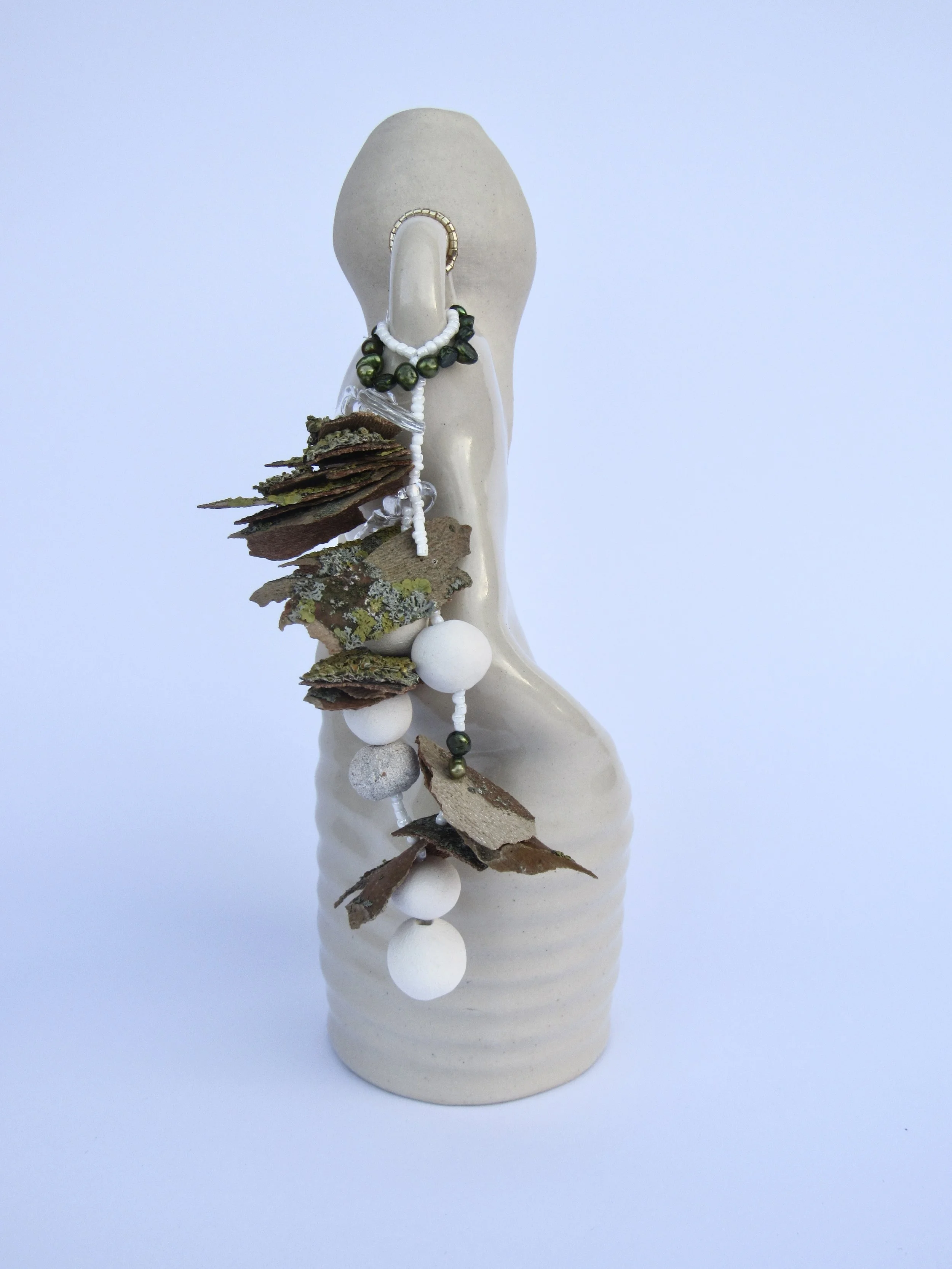 A beige decorative vase with a narrow neck, decorated with necklaces and natural elements like dried bark and moss, set against a light blue background.