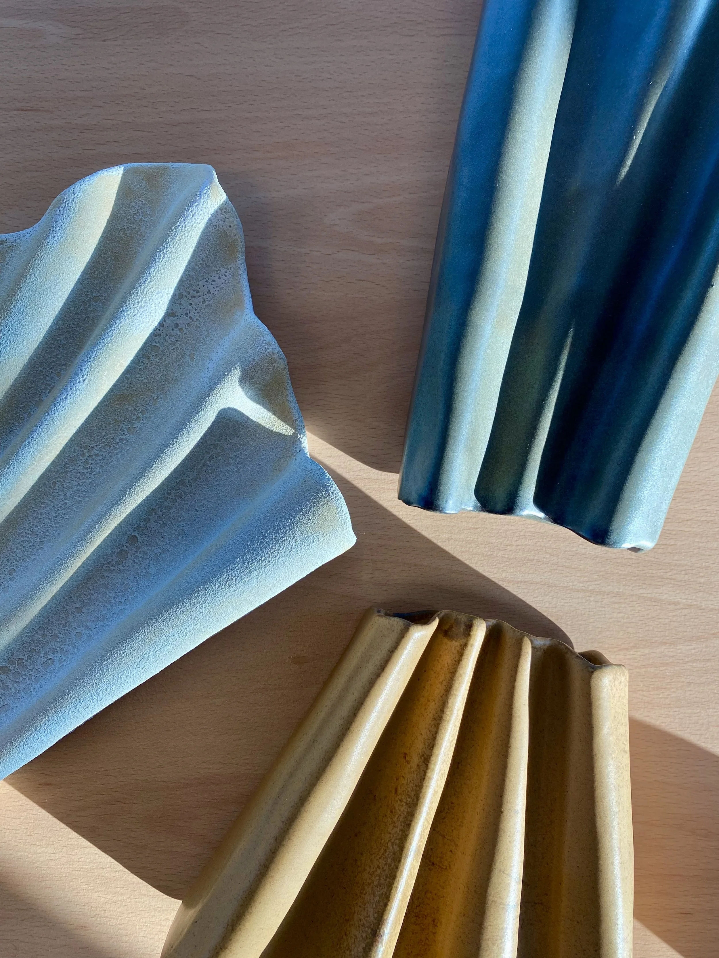 Close-up of various ceramic vases with ridges and textured surfaces in blue, yellow, and beige colors on a wooden surface.