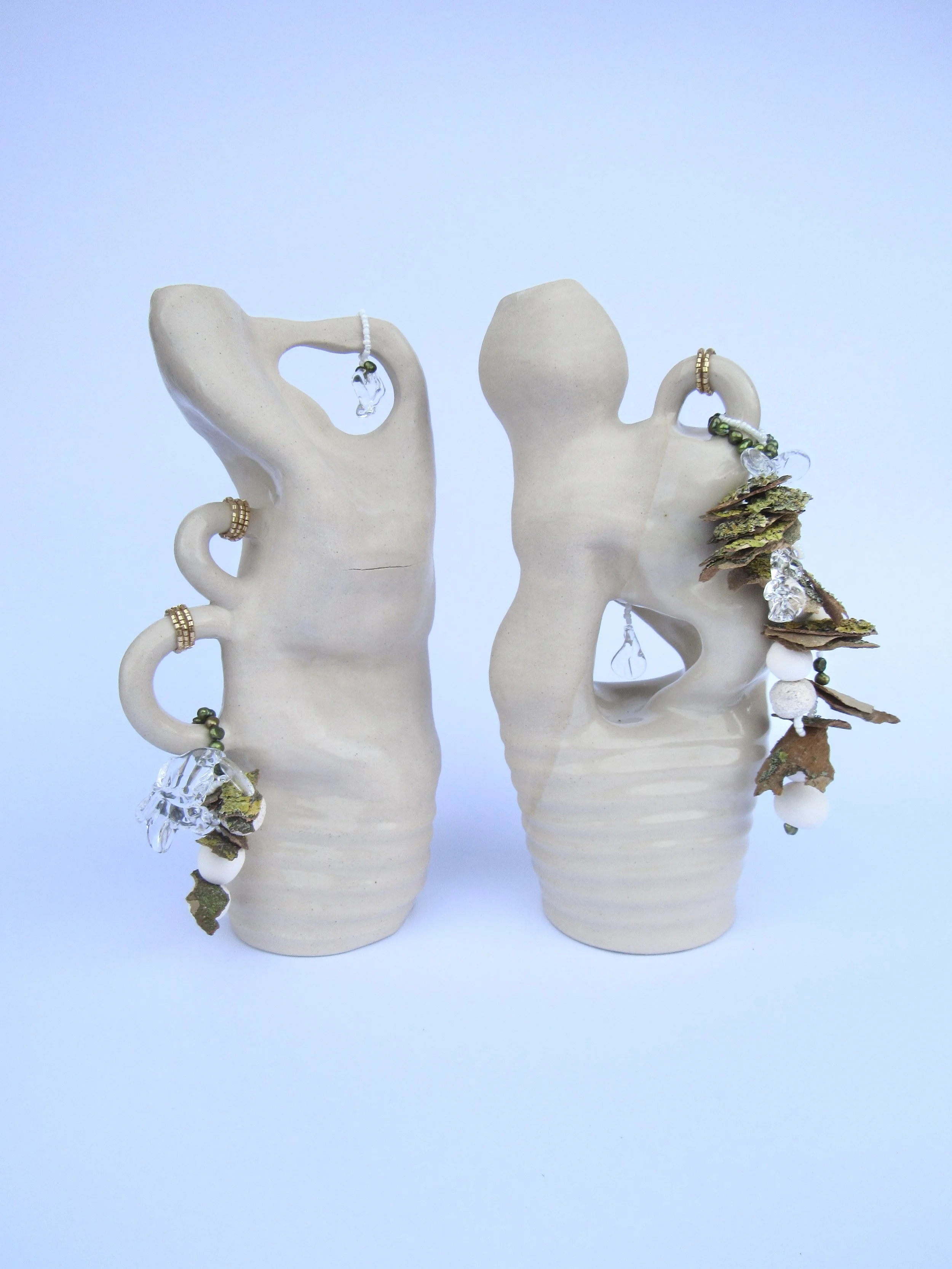 Two beige ceramic hand sculptures with jewelry and decorative elements, against a light blue background.