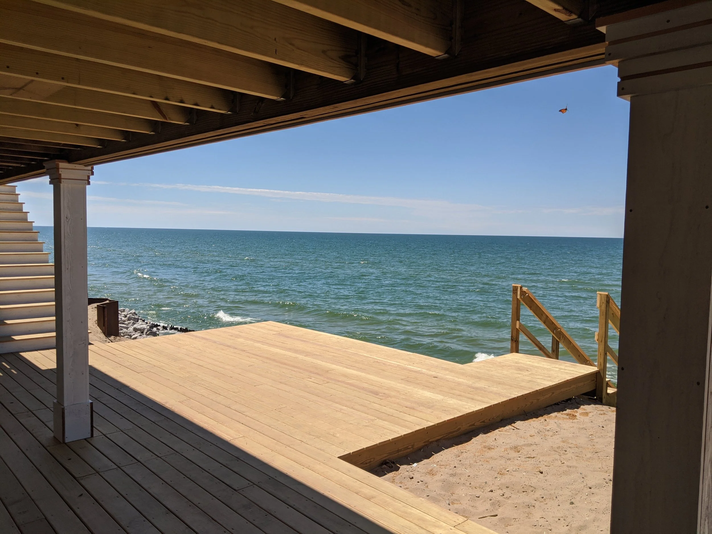 View from under a wooden pier looking out to the ocean with clear blue sky and a single butterfly flying.