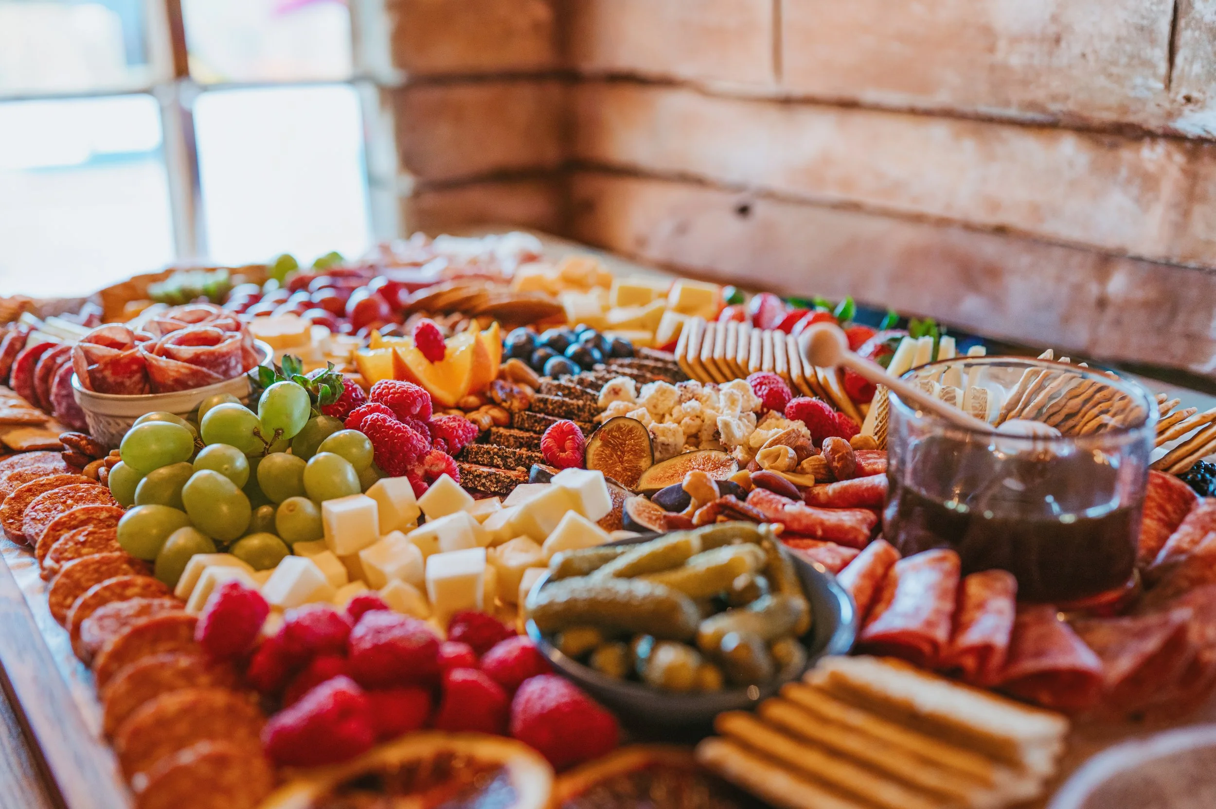 Assorted charcuterie board with cheese, fruits, nuts, crackers, and dips on a wooden table.