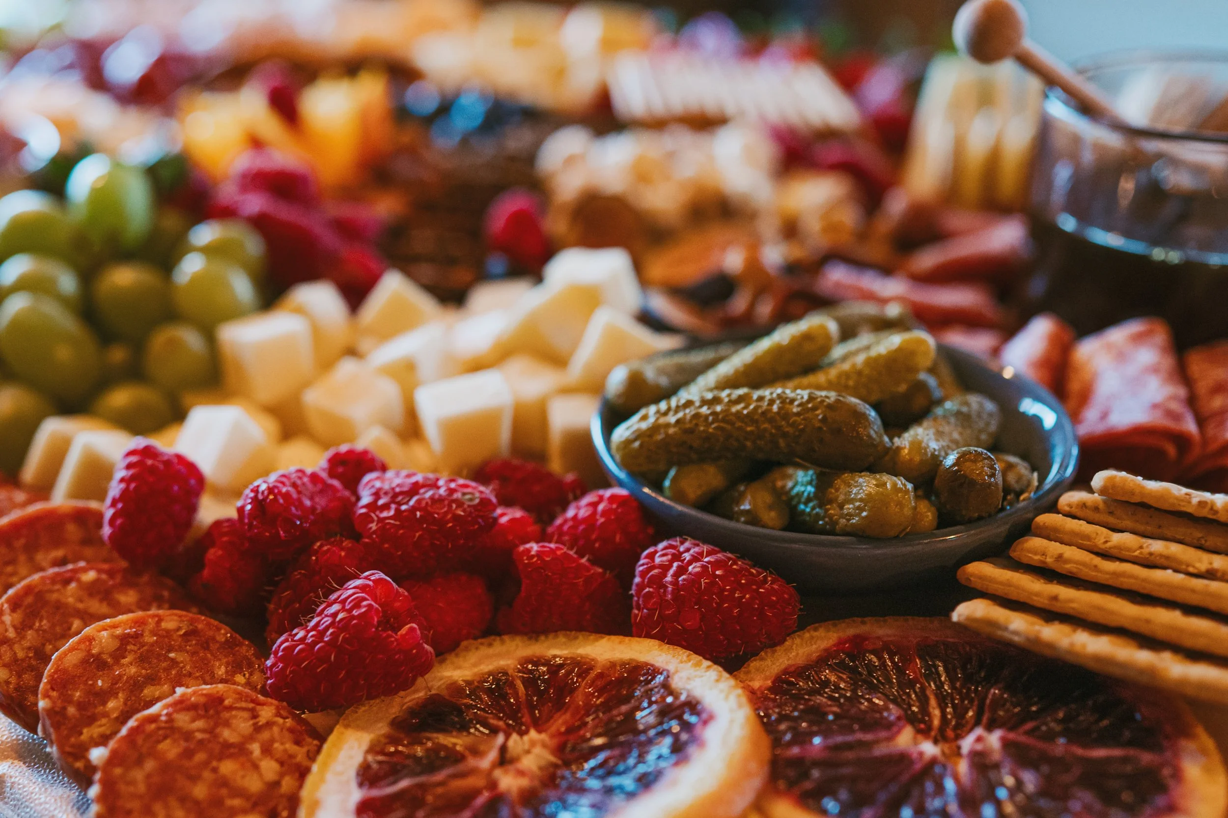A close-up of a variety of desserts and snacks, including green grapes, white cheese cubes, raspberries, dried figs, and sliced dried oranges, arranged on a serving platter.