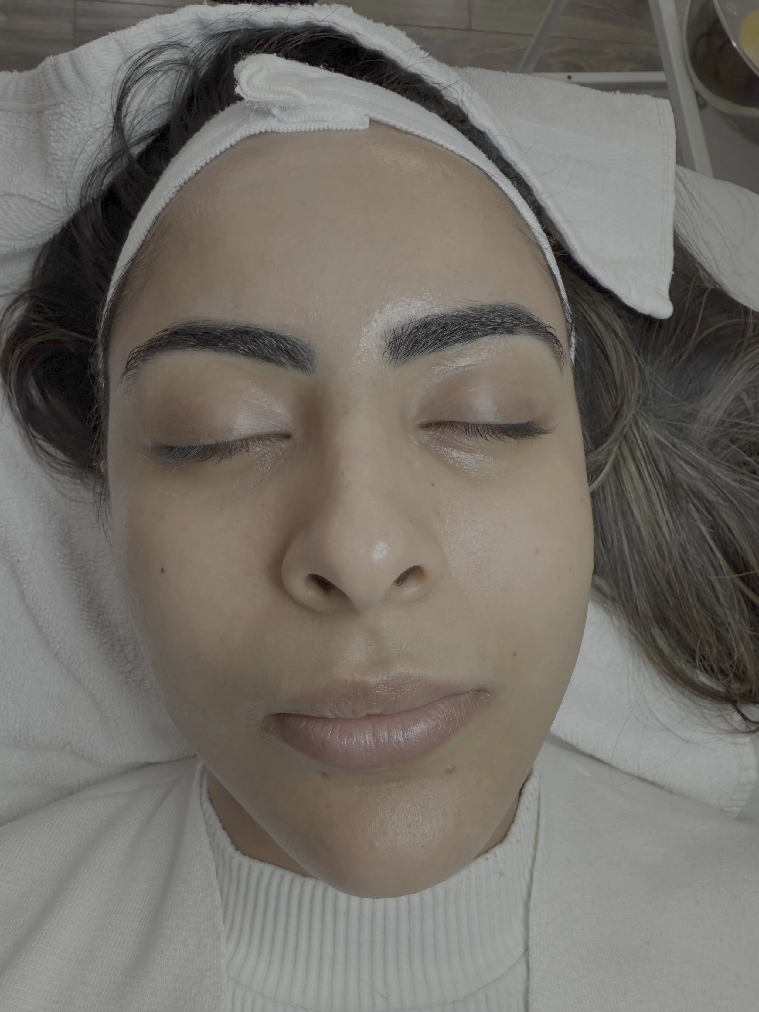 A woman with dark hair, laid back with closed eyes, appears to be receiving a beauty treatment or facial at a salon or spa.