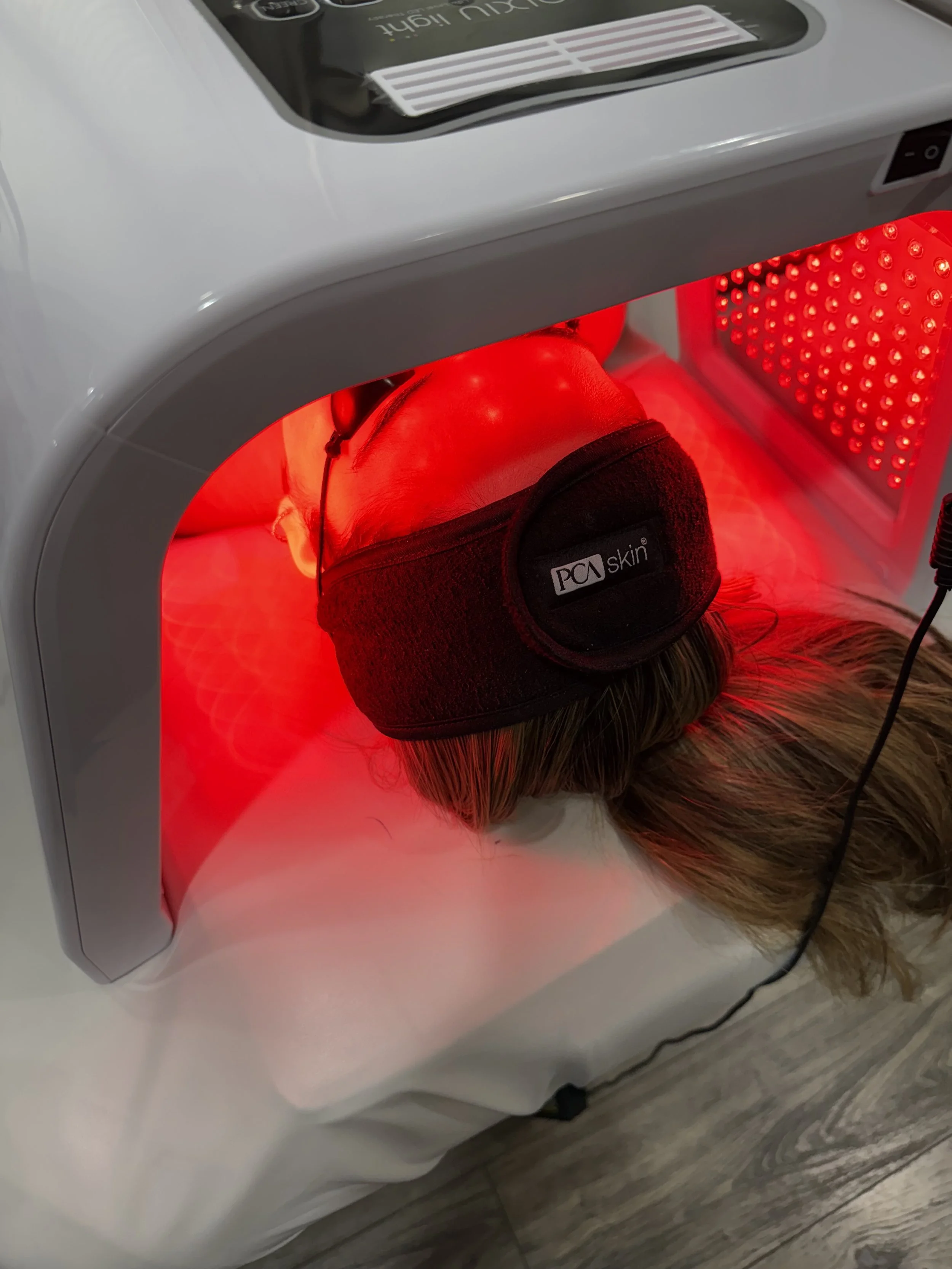 Person's head inside a red LED light therapy machine wearing a black PCA skin headband.