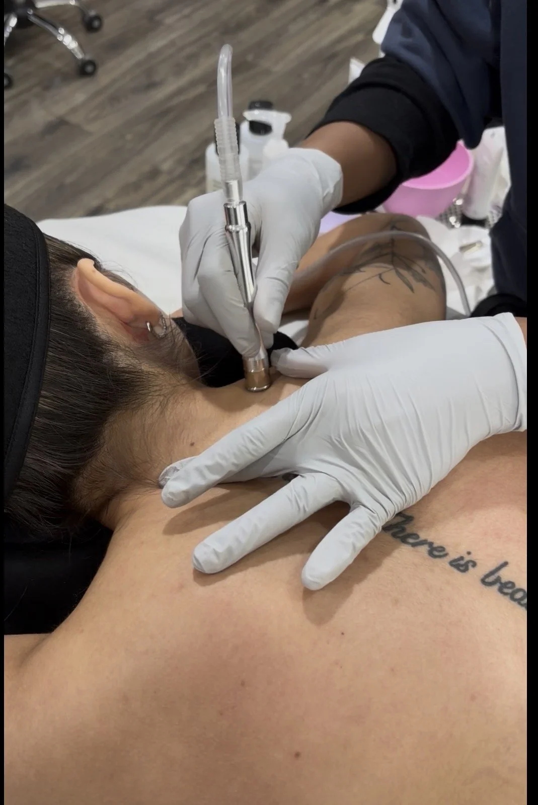 A person is receiving a tattoo on their upper chest with a tattoo machine operated by a tattoo artist wearing gloves, while the person is lying on a table.