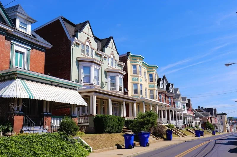 Row of colorful Victorian-style houses on a sunny street with blue sky.