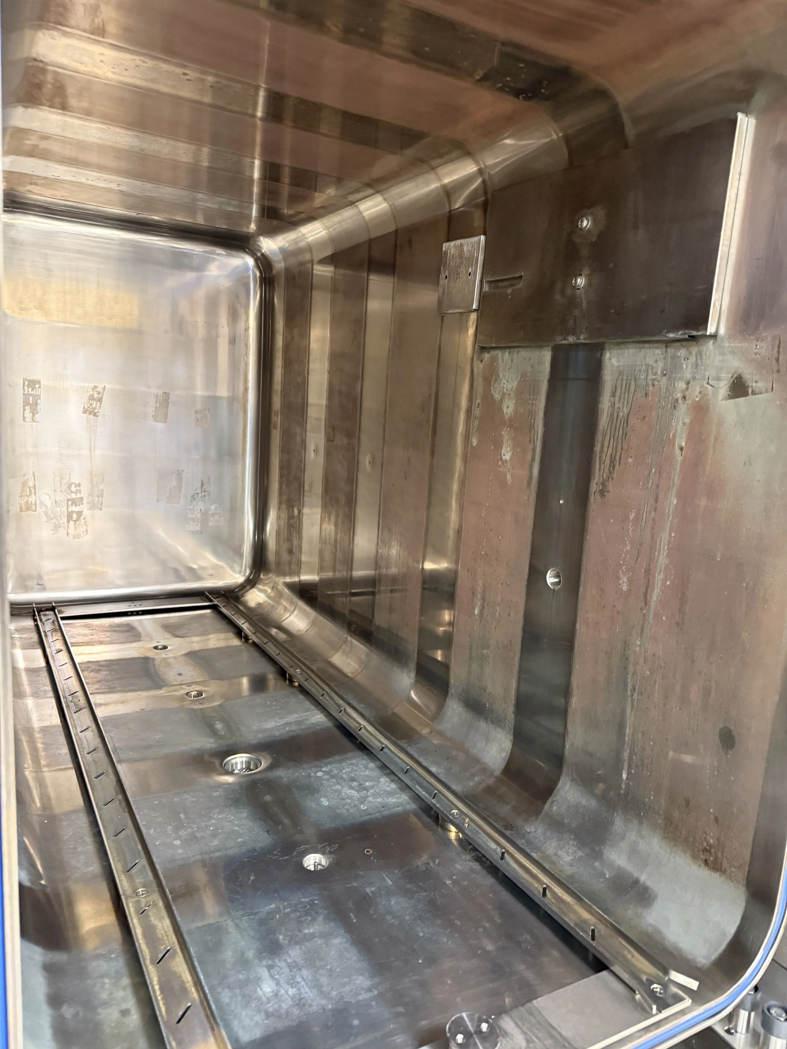 Inside view of a heavily bioburdened stainless steel autoclave with a large rectangular inner chamber, small holes, and a sliding rail or track at the bottom.