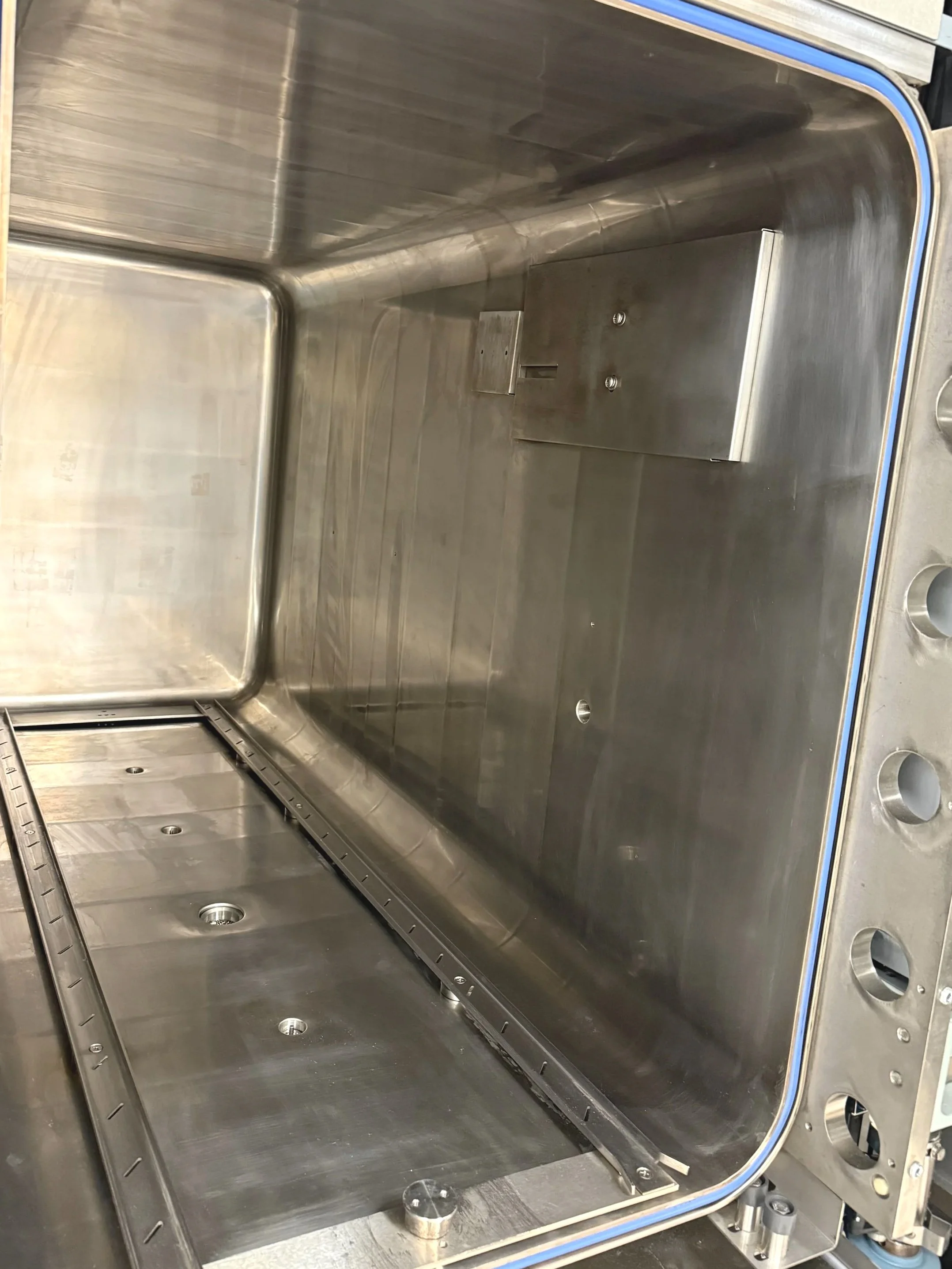 Inside an empty stainless steel sterilizer that has been proficiently cleaned with rounded edges and multiple holes for fixtures or attachments.