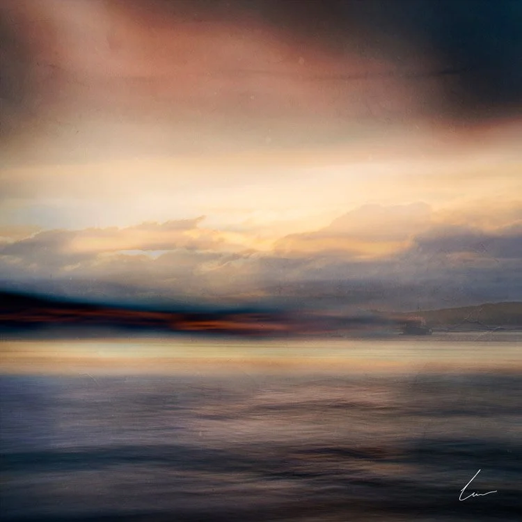 A blurred landscape of a sunset over a body of water with mountains in the distance, featuring a colorful sky with clouds and warm tones.