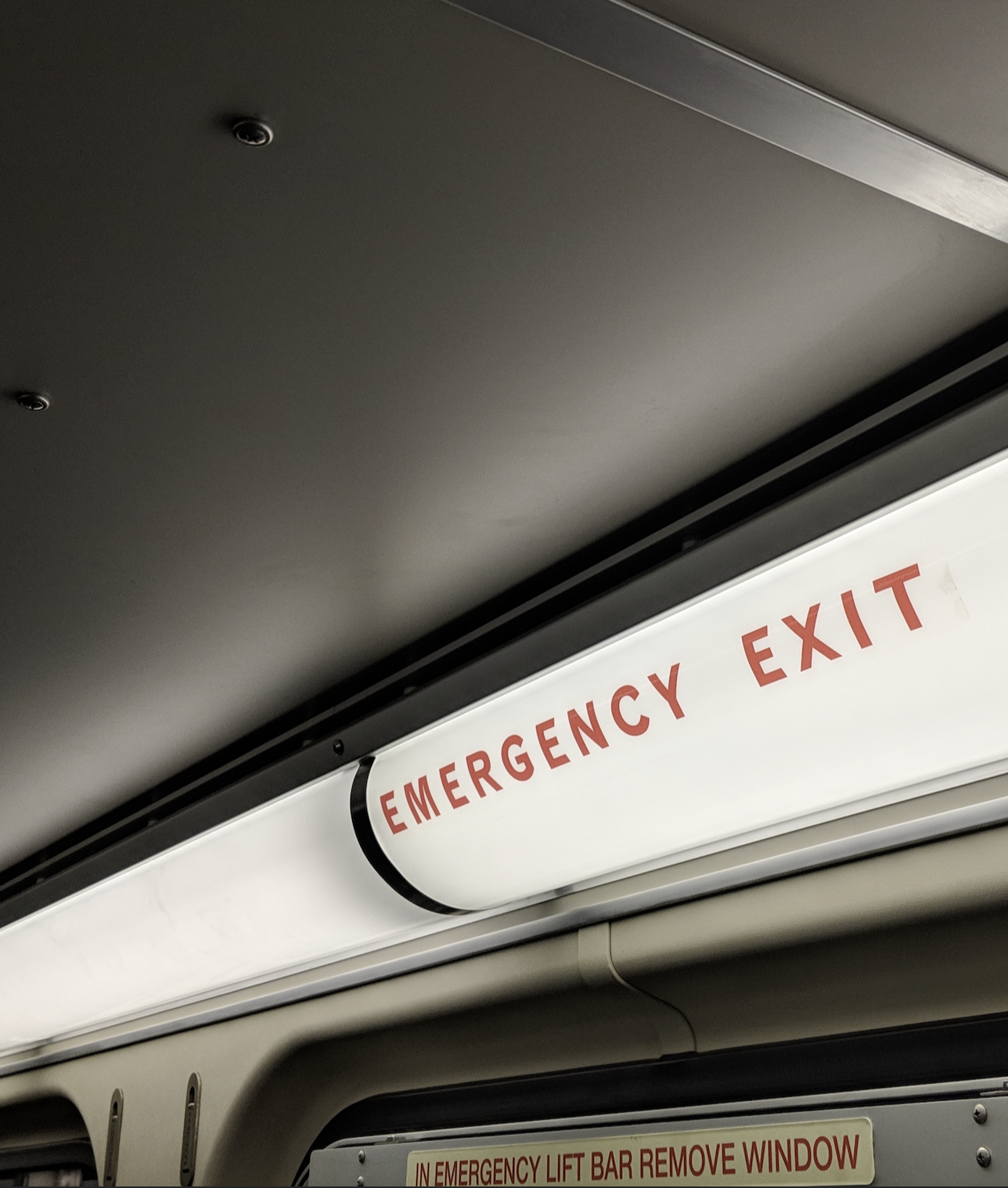 Close-up of an illuminated emergency exit sign in a building, with red text on a white background.