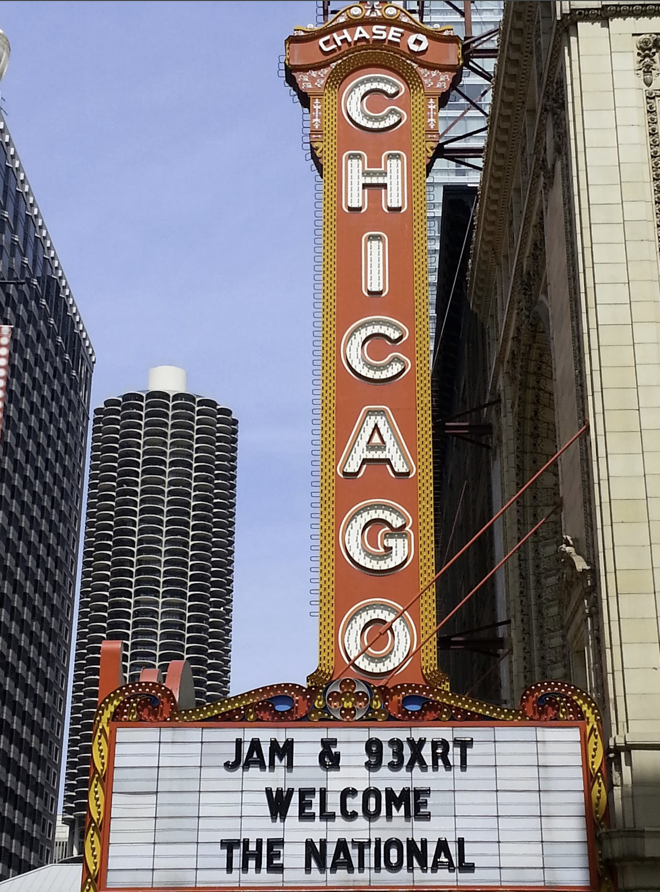 Chase Chicago theater marquee with a red and yellow vertical sign. The marquee displays an event with jam and 93XRT radio station, with a welcome message for the national event. Tall buildings are seen in the background against a clear blue sky.