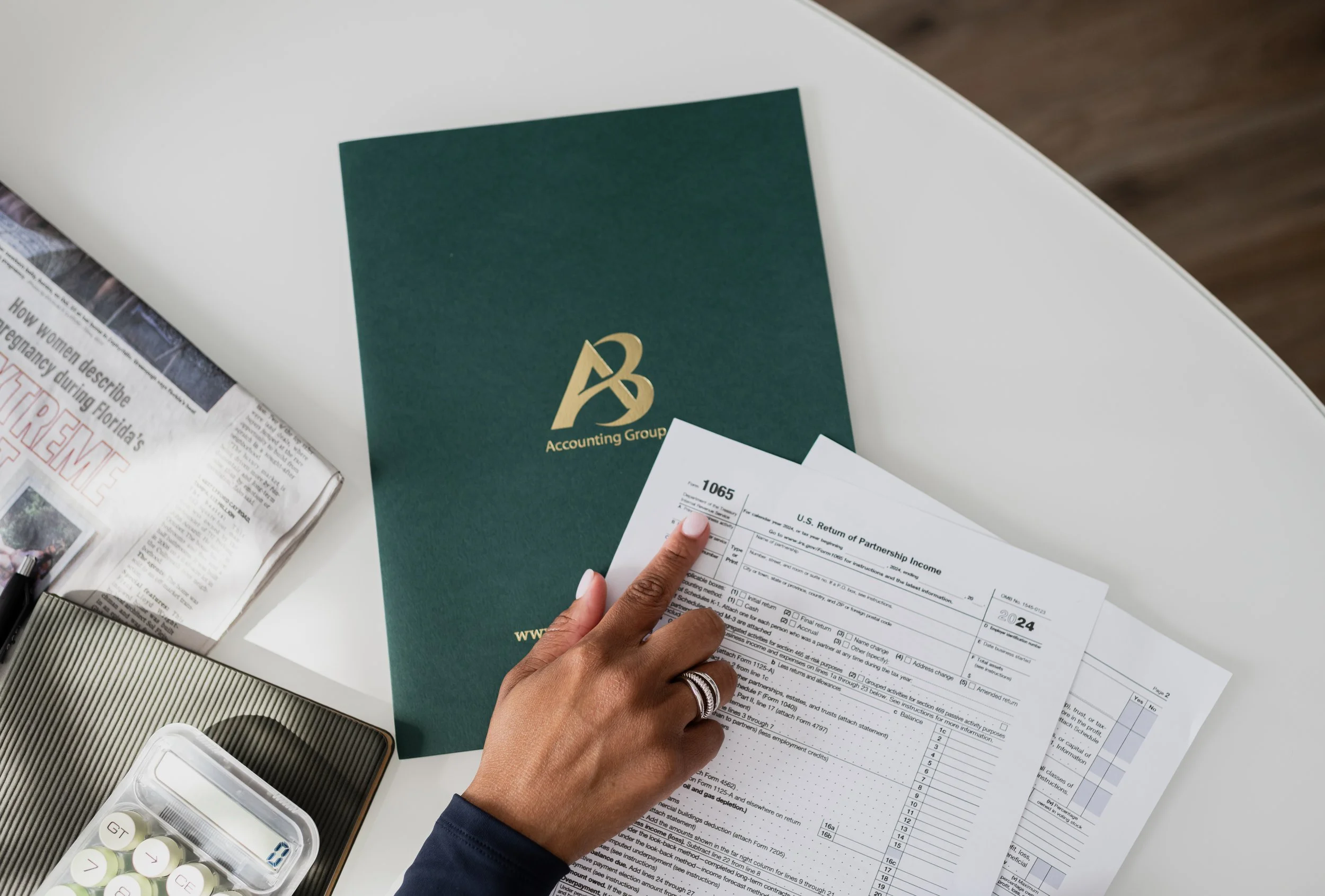 A person holding a tax form, with a green accounting booklet and various papers and supplies on a white desk.