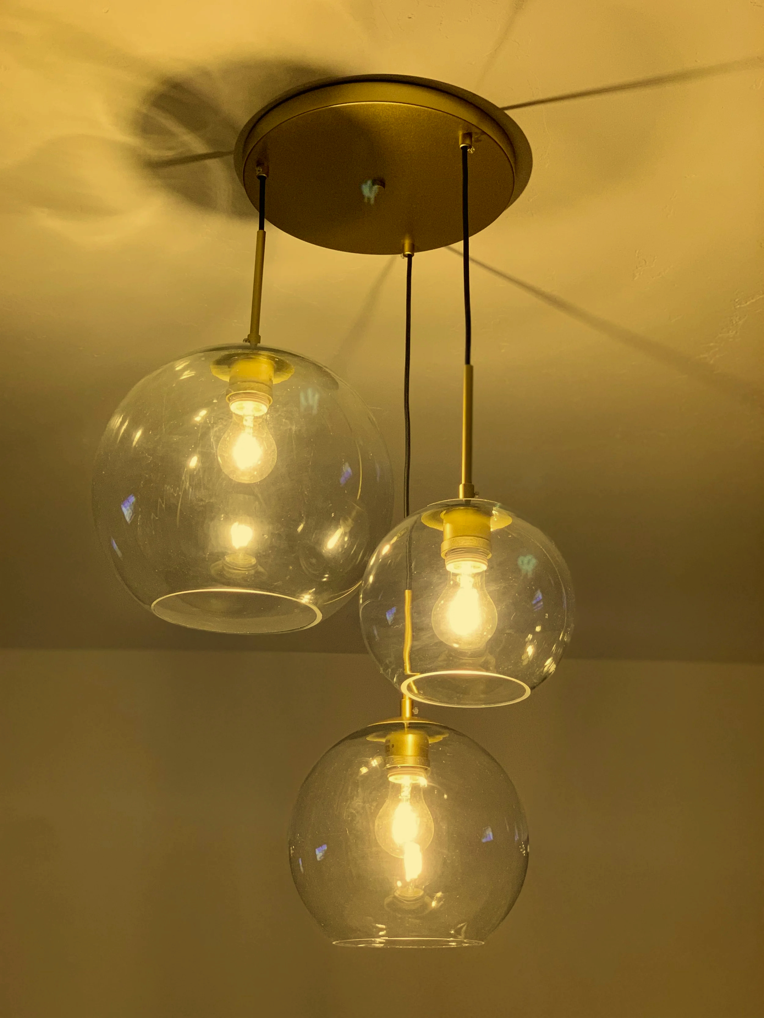 A ceiling light fixture with three hanging glass globes, each containing a light bulb illuminated inside, attached to a gold-colored base.