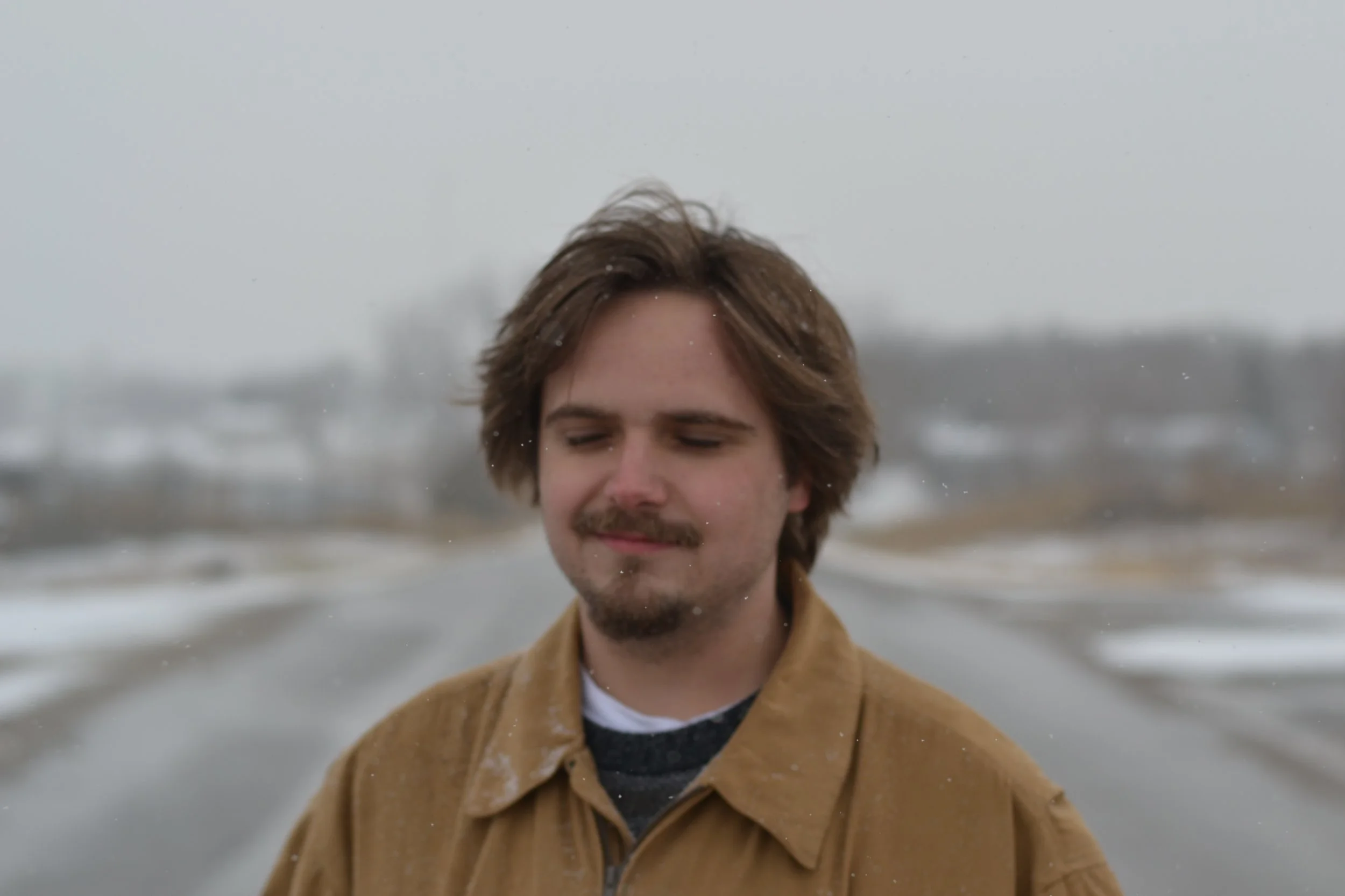 Ryan Christopher Park stands outdoors on a snowy day with a peaceful expression and eyes closed. BTS photo from HOTHEADS (2025).