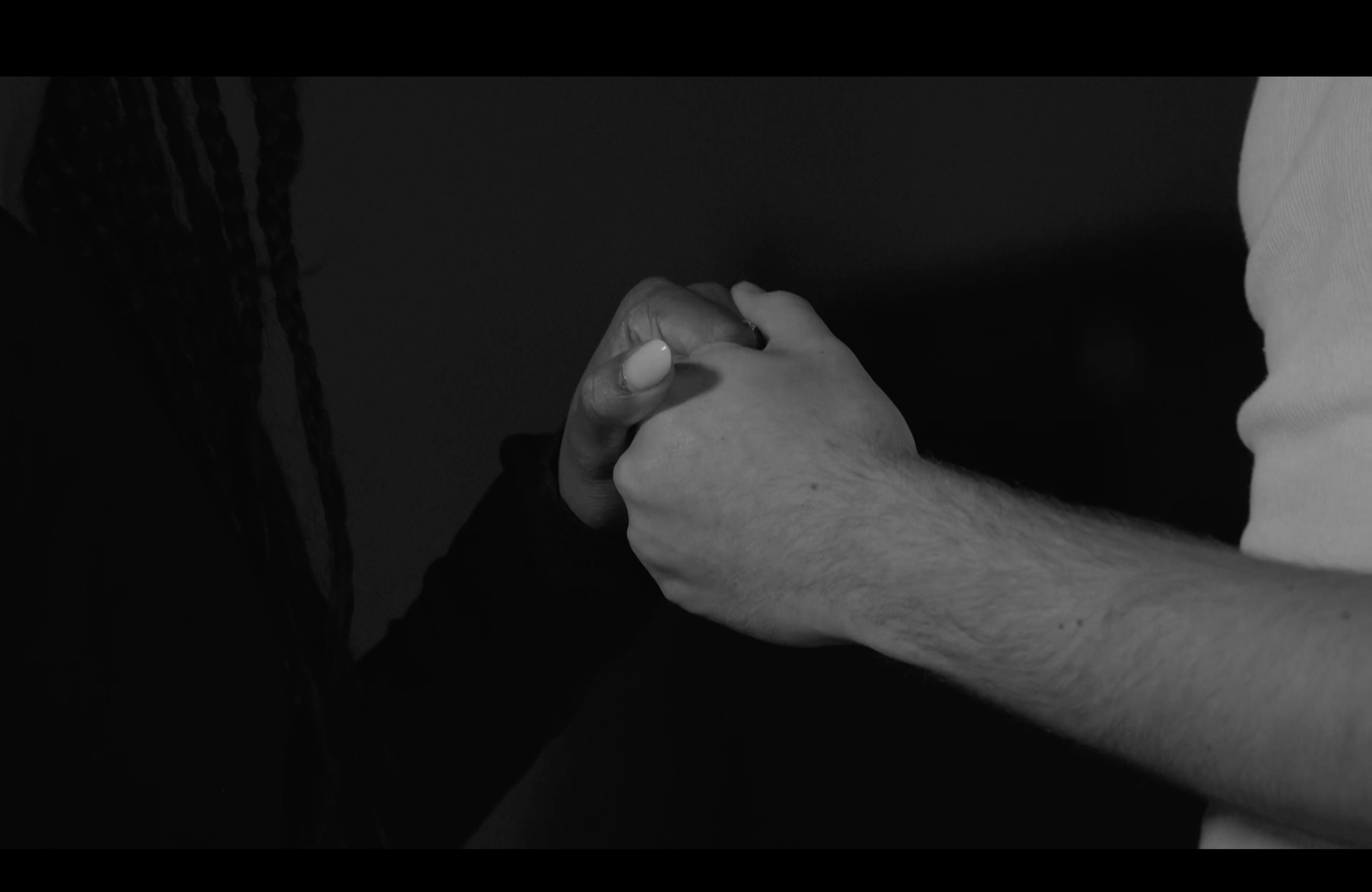 Close-up of a man and woman holding hands in a peaceful grasp. Still from the short film, THE IRON BULL (2024).