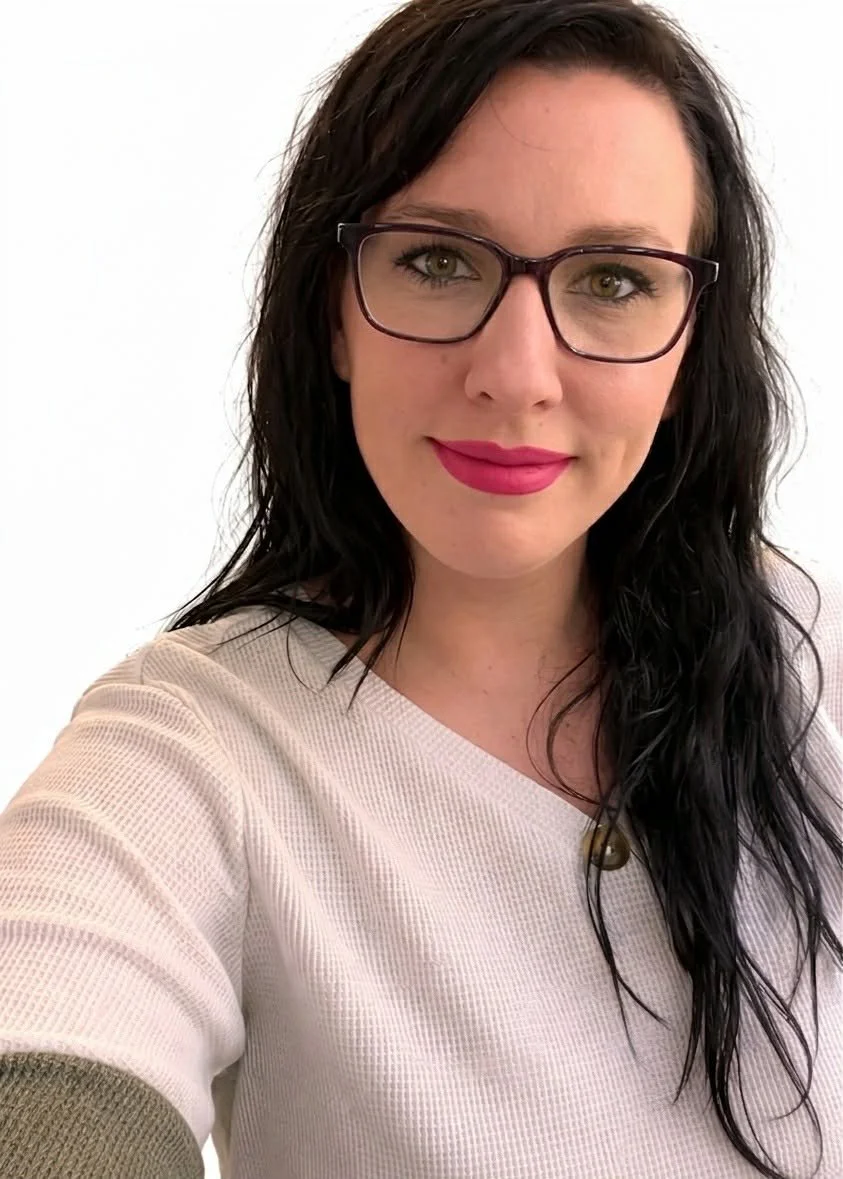 Une femme avec des lunettes noires et des cheveux noirs, portant un haut blanc.