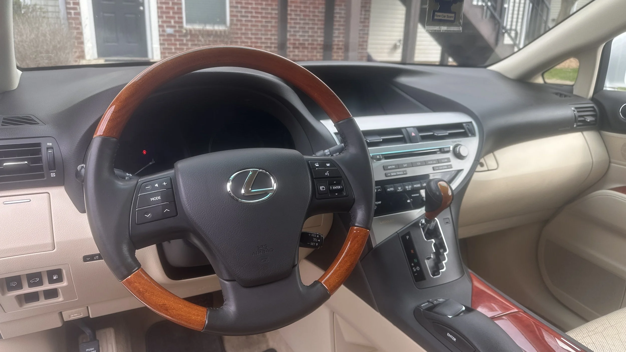 Interior of a Lexus vehicle showing the steering wheel, dashboard, and gear shift lever. The steering wheel has a wood finish with the Lexus logo in the center.