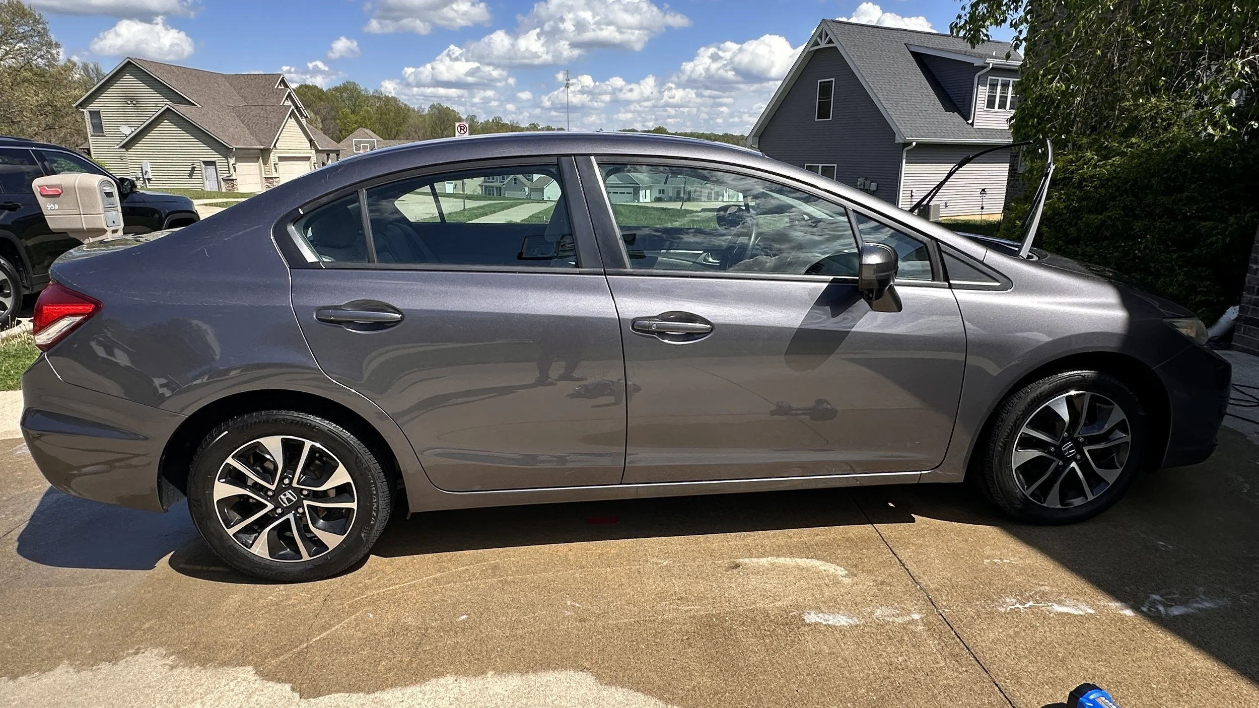 A gray Honda sedan parked outside with houses and a blue sky in the background.