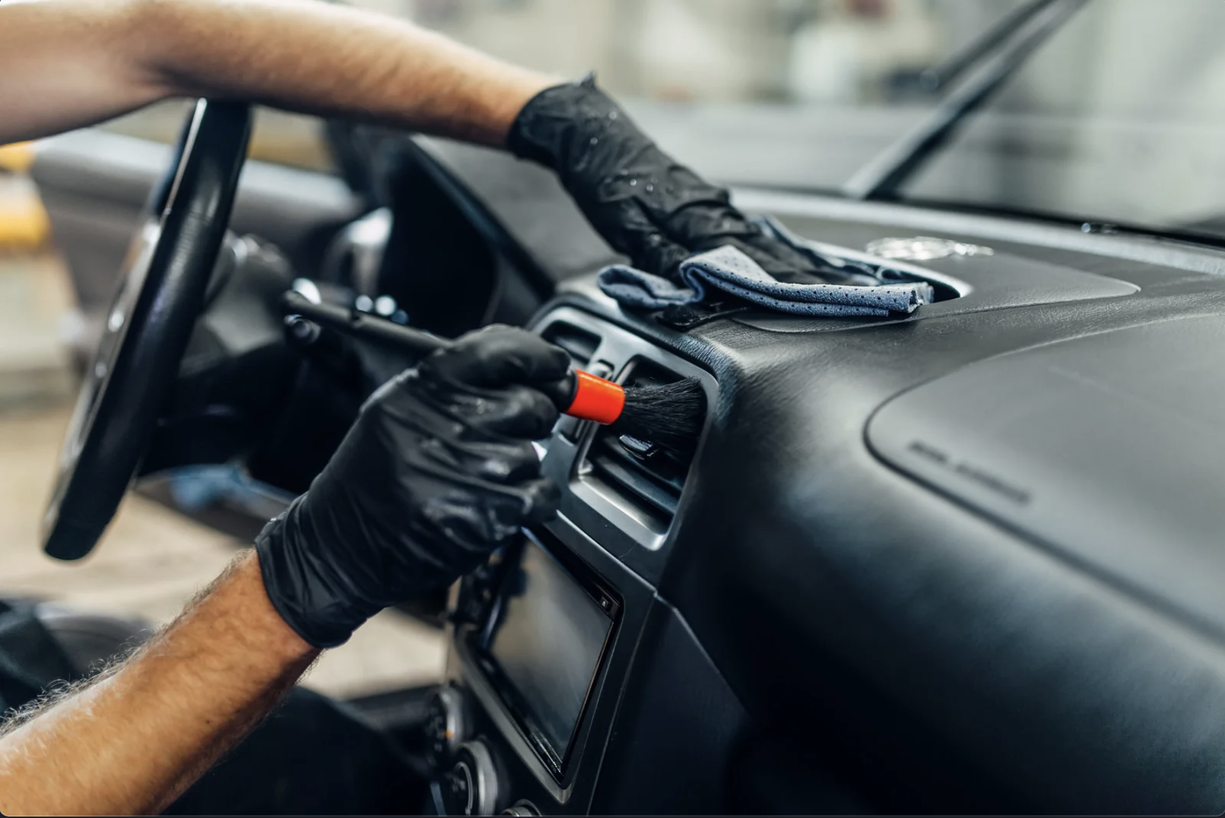 Person cleaning the car's air vent with a brush and wearing black gloves.