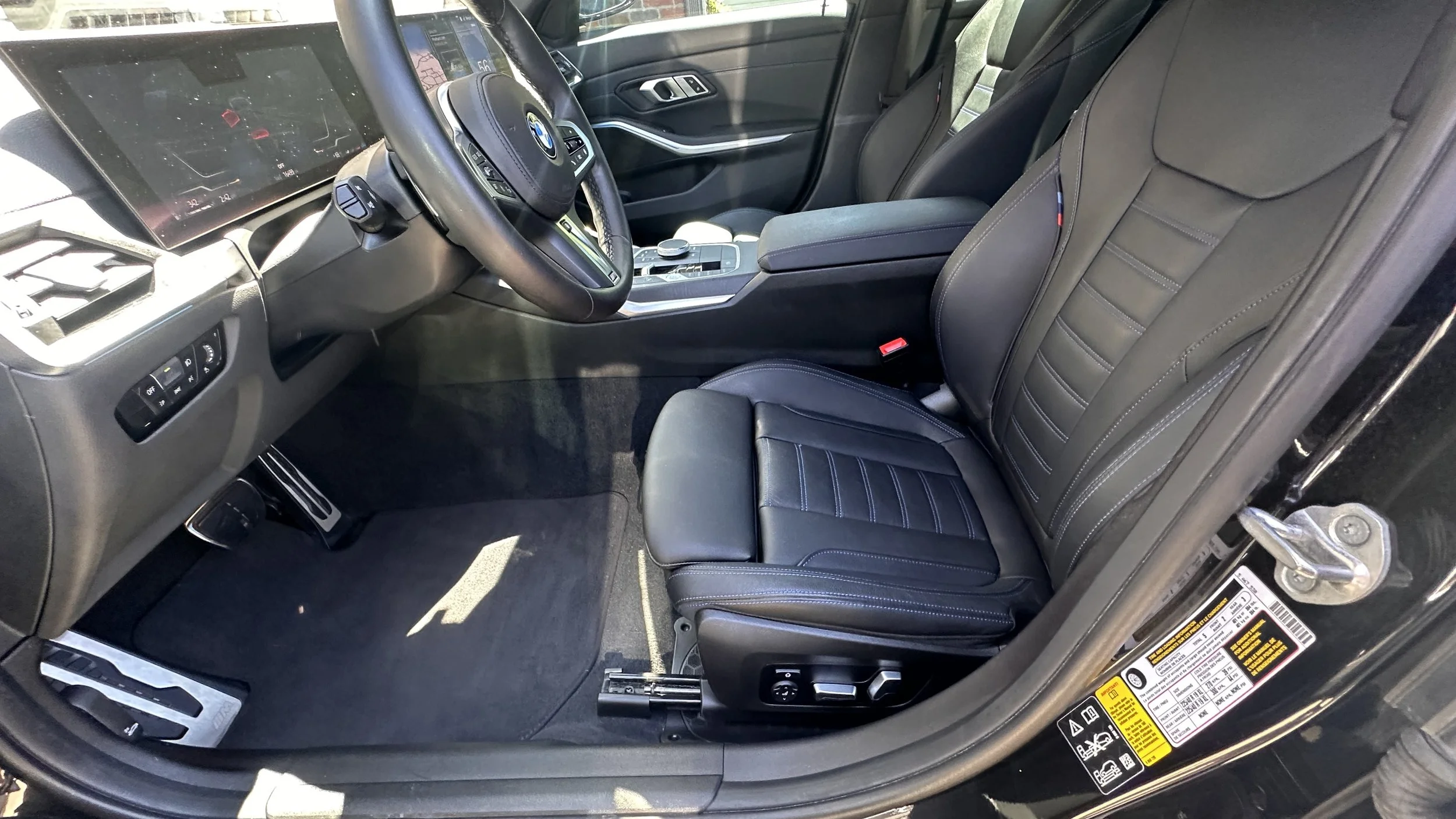 Interior of a BMW vehicle showing black leather front and back seats, dashboard, and center console, with sunlight illuminating the interior.