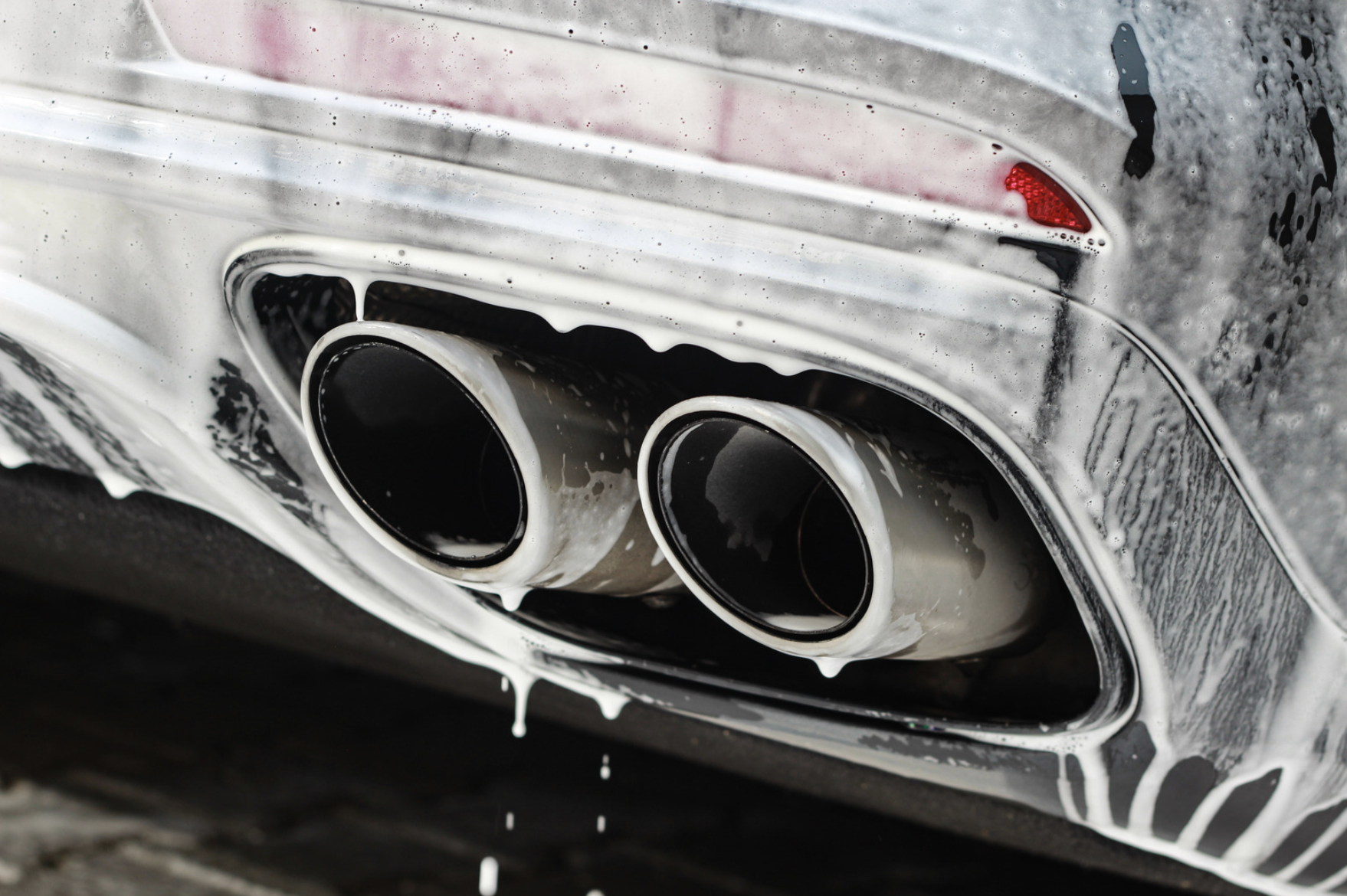 Close-up of a car's dual exhaust pipes with soapy foam and water drips.
