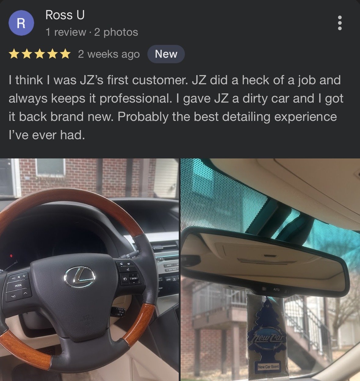 Interior view of a Lexus car, showing a steering wheel with wood trim and the dashboard, and a rearview mirror with a New Car Scent air freshener hanging.