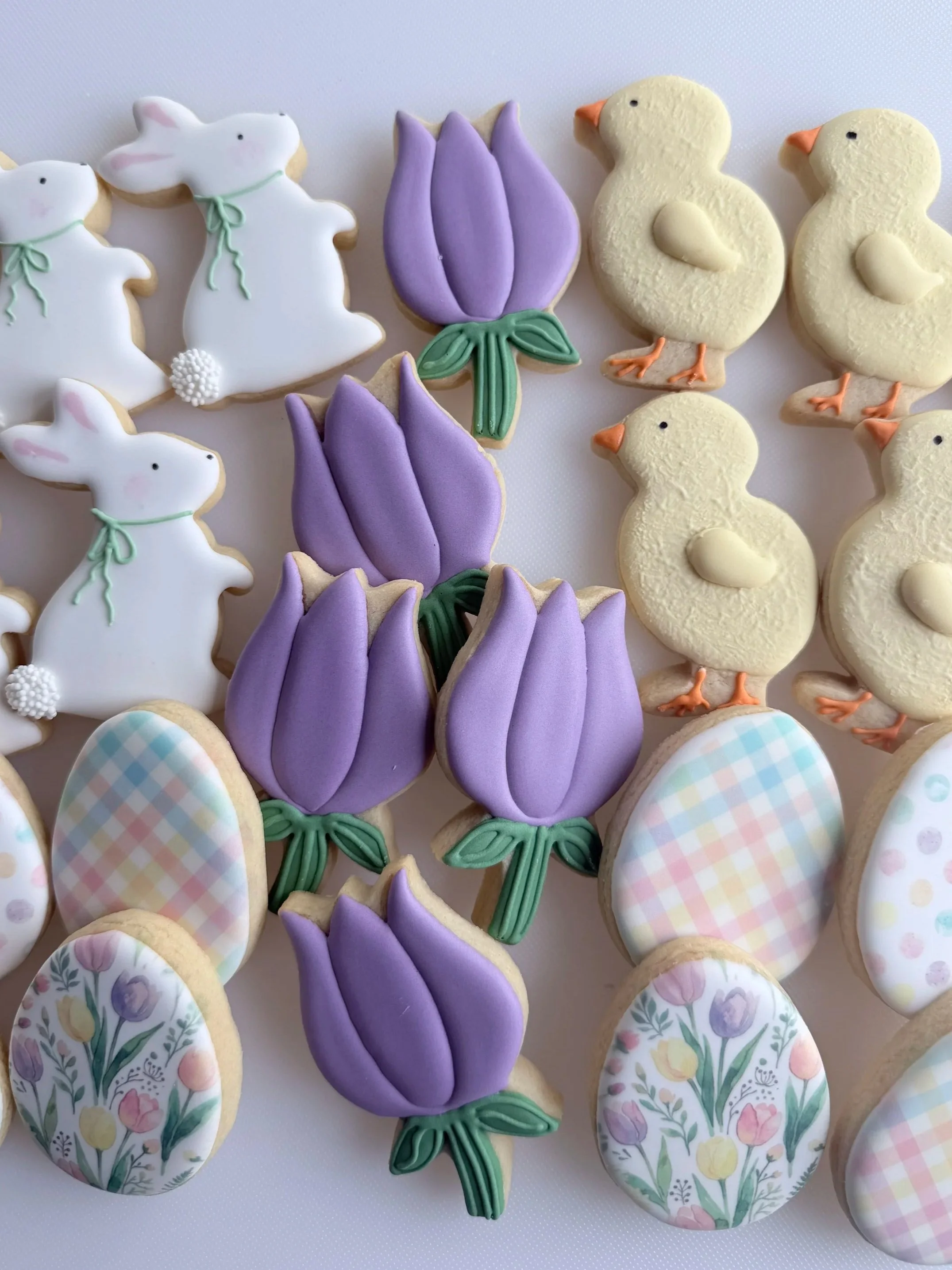 Decorated sugar cookies in Easter motifs: rabbits, a purple tulip, ducklings, and pastel checkered eggs.