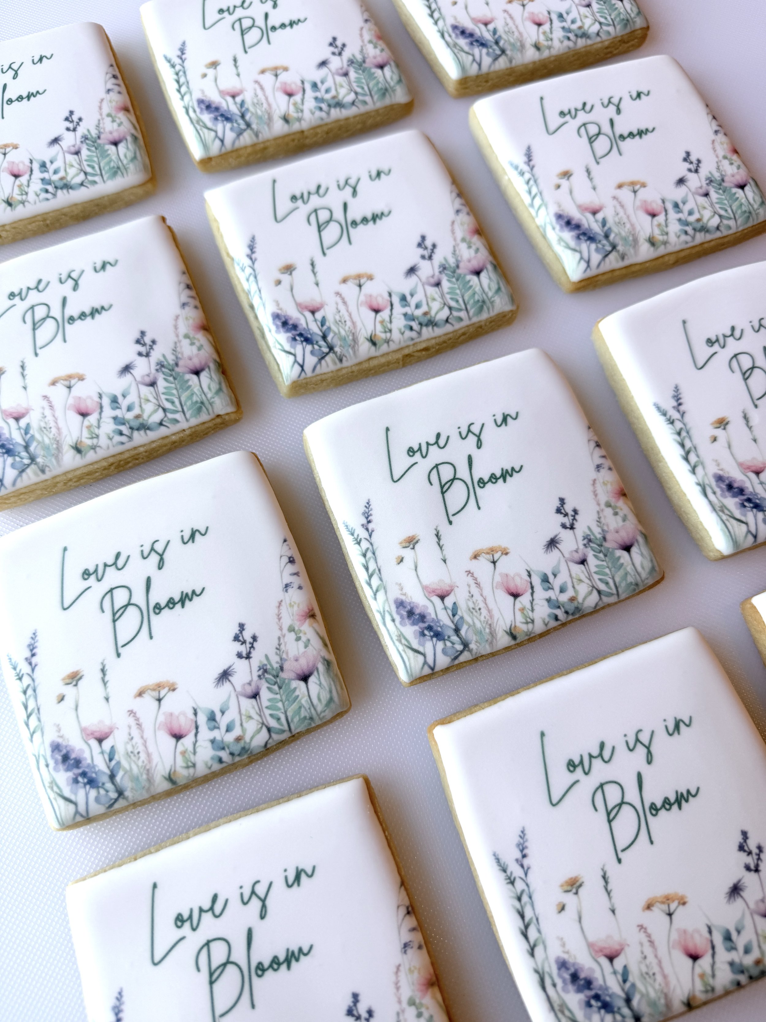 Decorative cookies with floral designs and the phrase 'Love is in Bloom' written in green, arranged on a light surface.