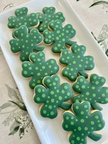 Cookies shaped like shamrocks decorated with green icing and green polka dots, arranged on a white plate.