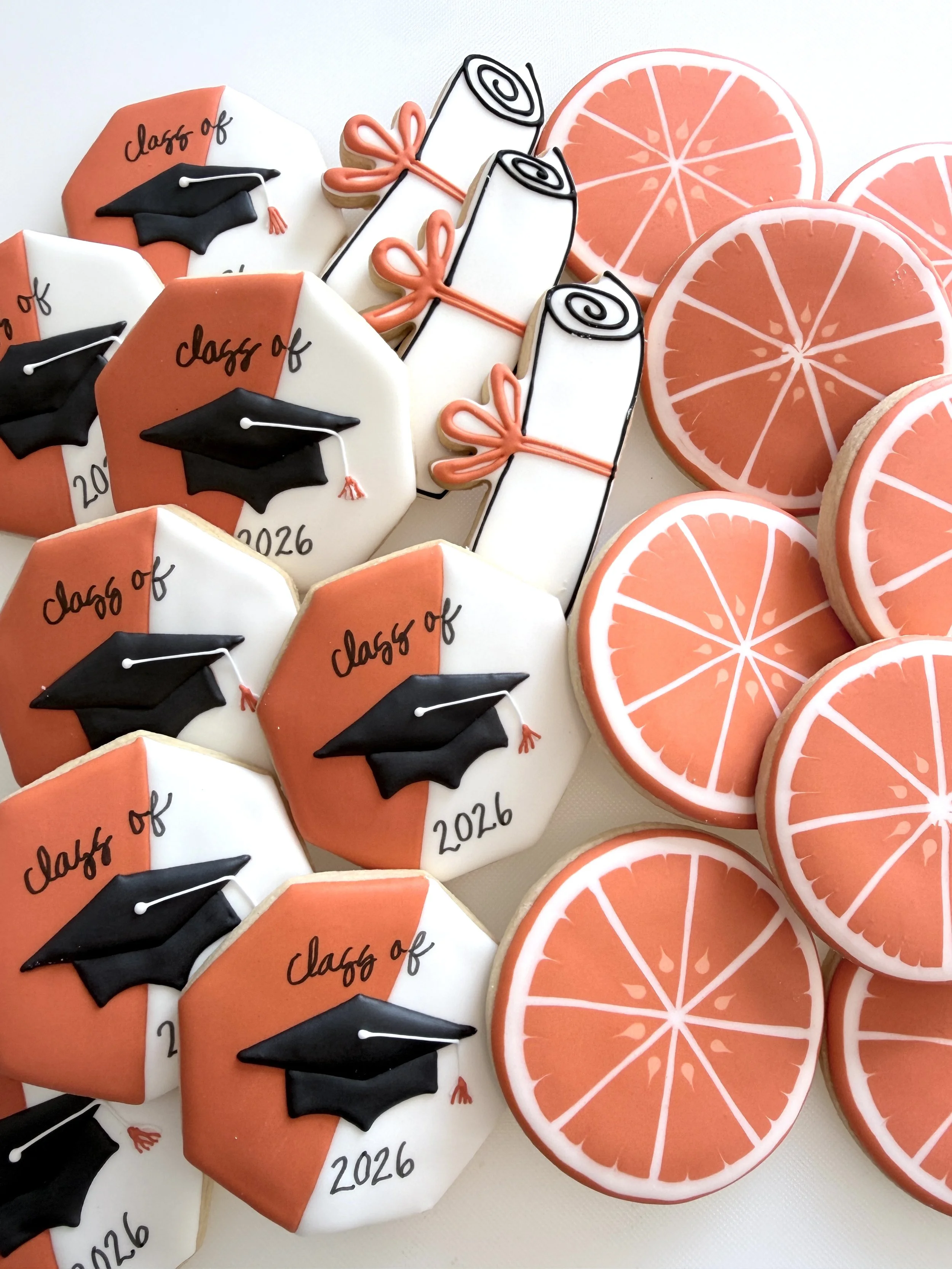 Decorated cookies with graduation caps, scrolls tied with pink ribbons, and grapefruit slices.