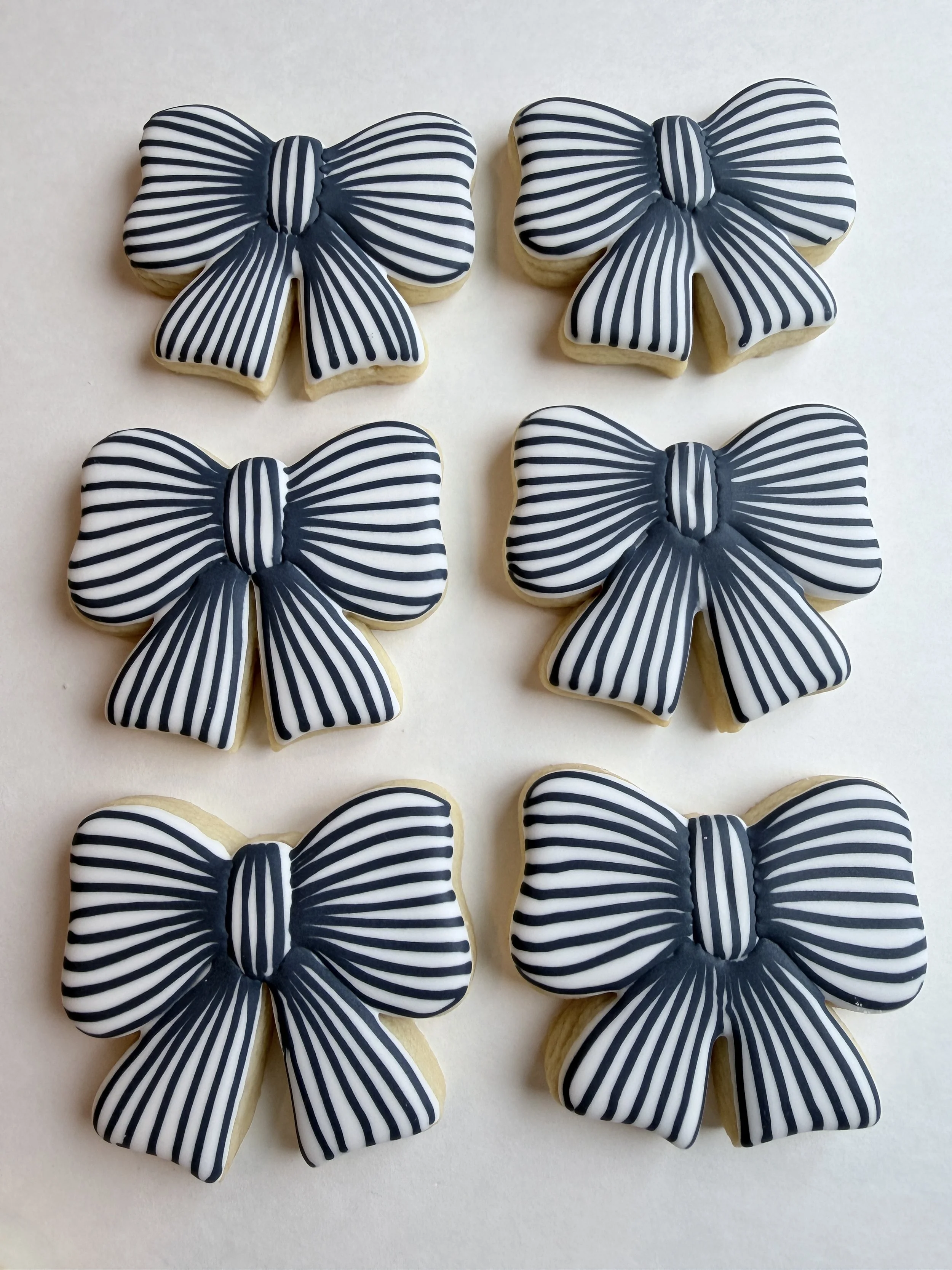 Four sugar cookies decorated with black and white striped bows on a white surface.