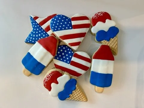 Patriotic treats decorated with American flag themes, including popsicles, a heart, a star, and ice cream cones with red, white, and blue colors and patterns.