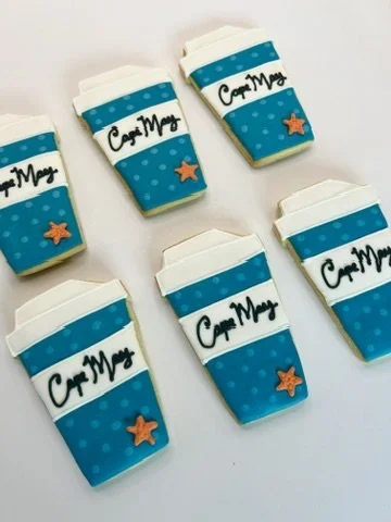Six decorated cookies shaped like coffee cups with blue dotted sleeves, white lids, and black 'Coffee Mug' text, each with an orange starfish decoration on the sleeve.