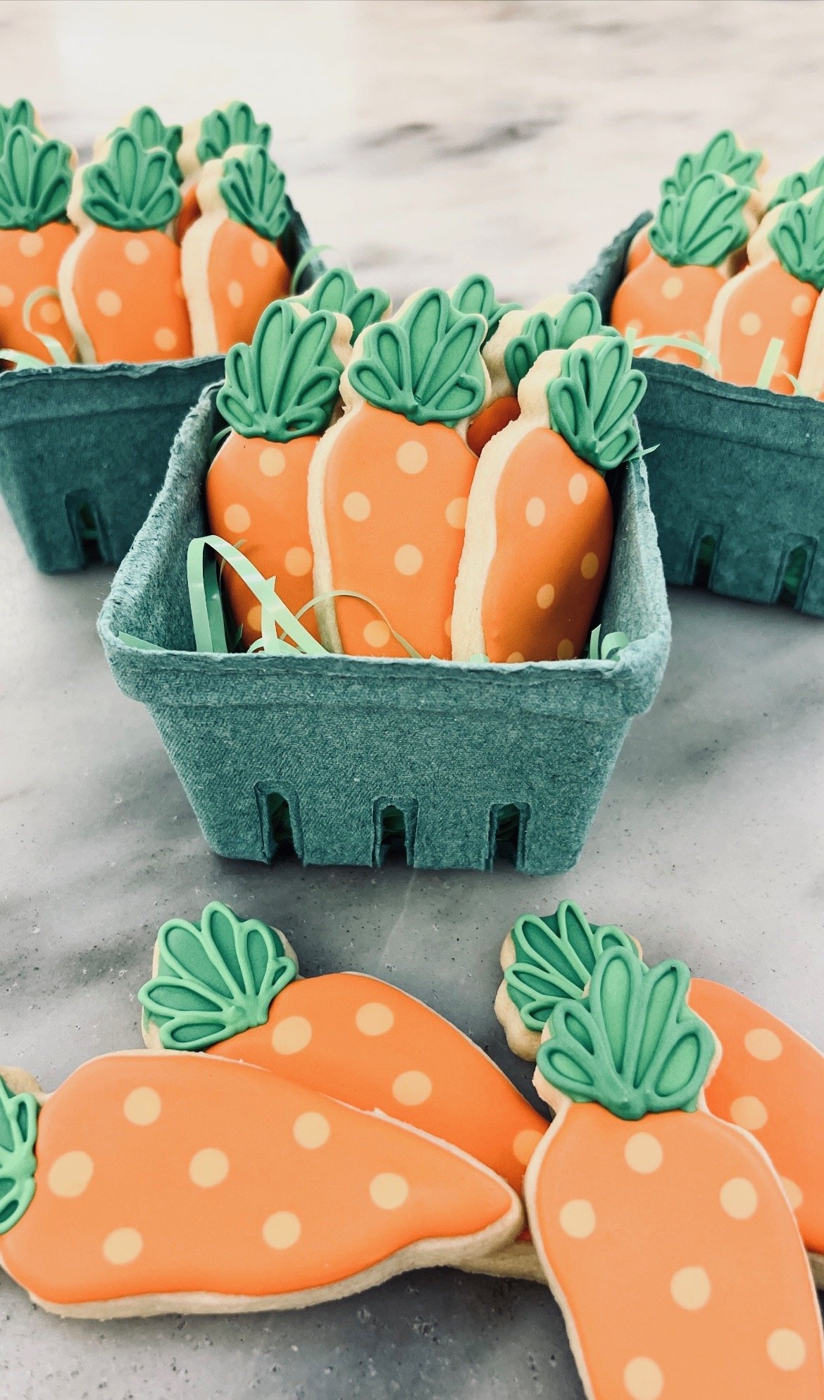 Decorative sugar cookies shaped and decorated like carrots with green leaves, arranged in teal muffin tins.