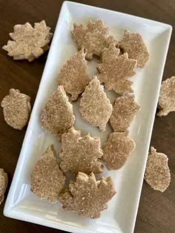 Sugar cookies in the shape of snowflakes on a white rectangular dish with some cookies scattered around.