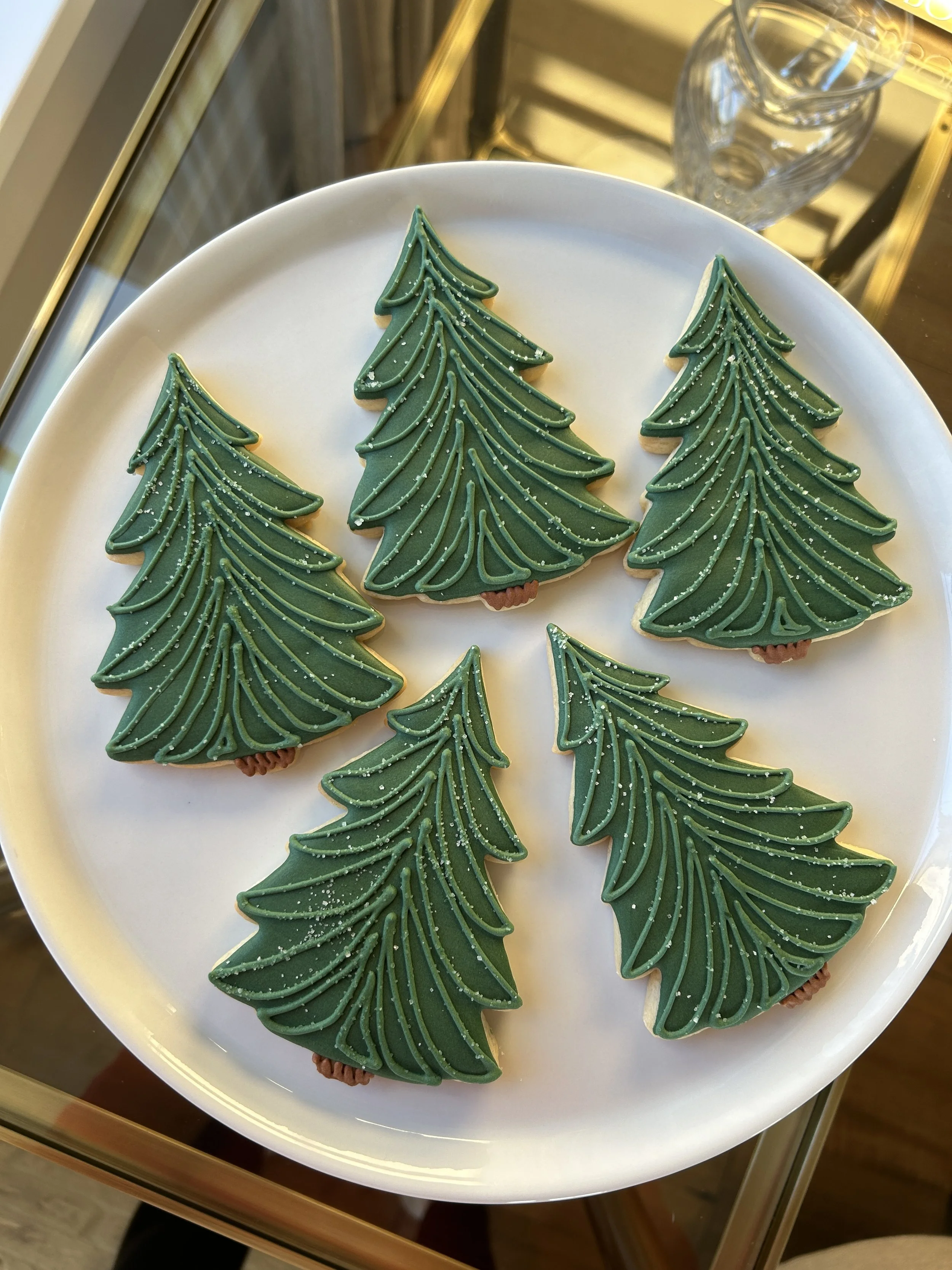 Christmas tree-shaped cookies decorated with green icing and small white sprinkles on a white plate.
