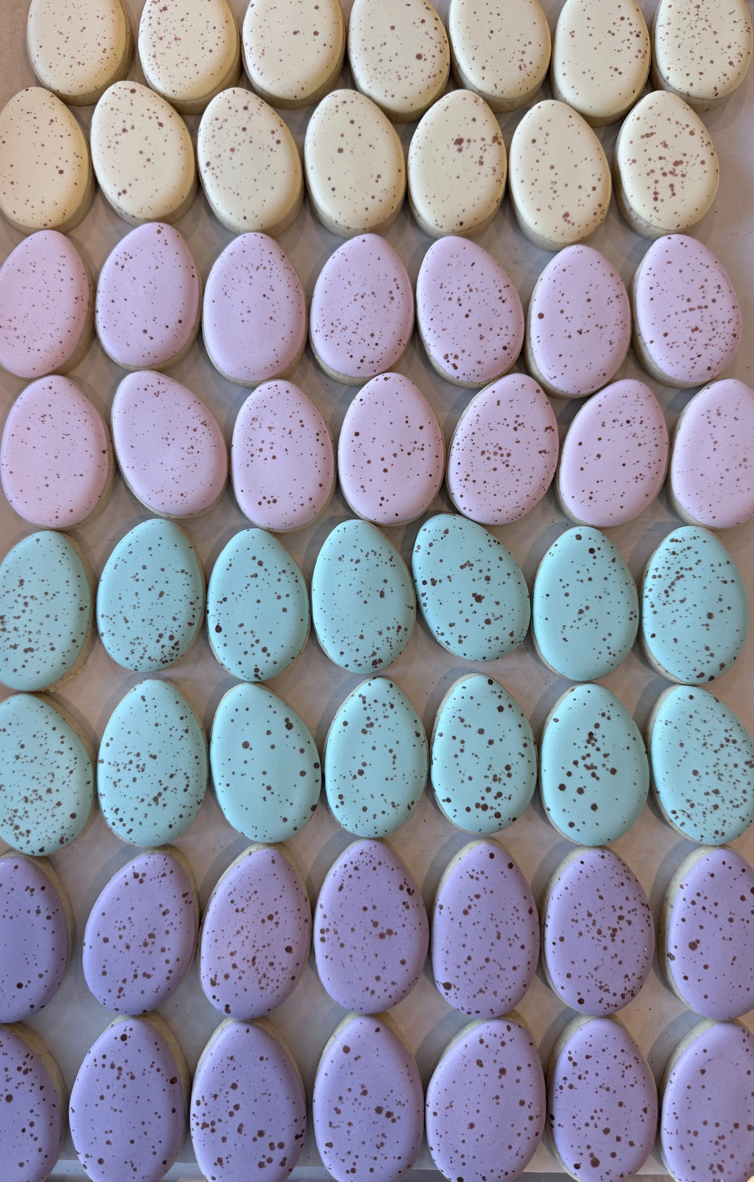 Colorful egg-shaped candies decorated with speckled designs in pastel pink, blue, and white colors arranged in rows.
