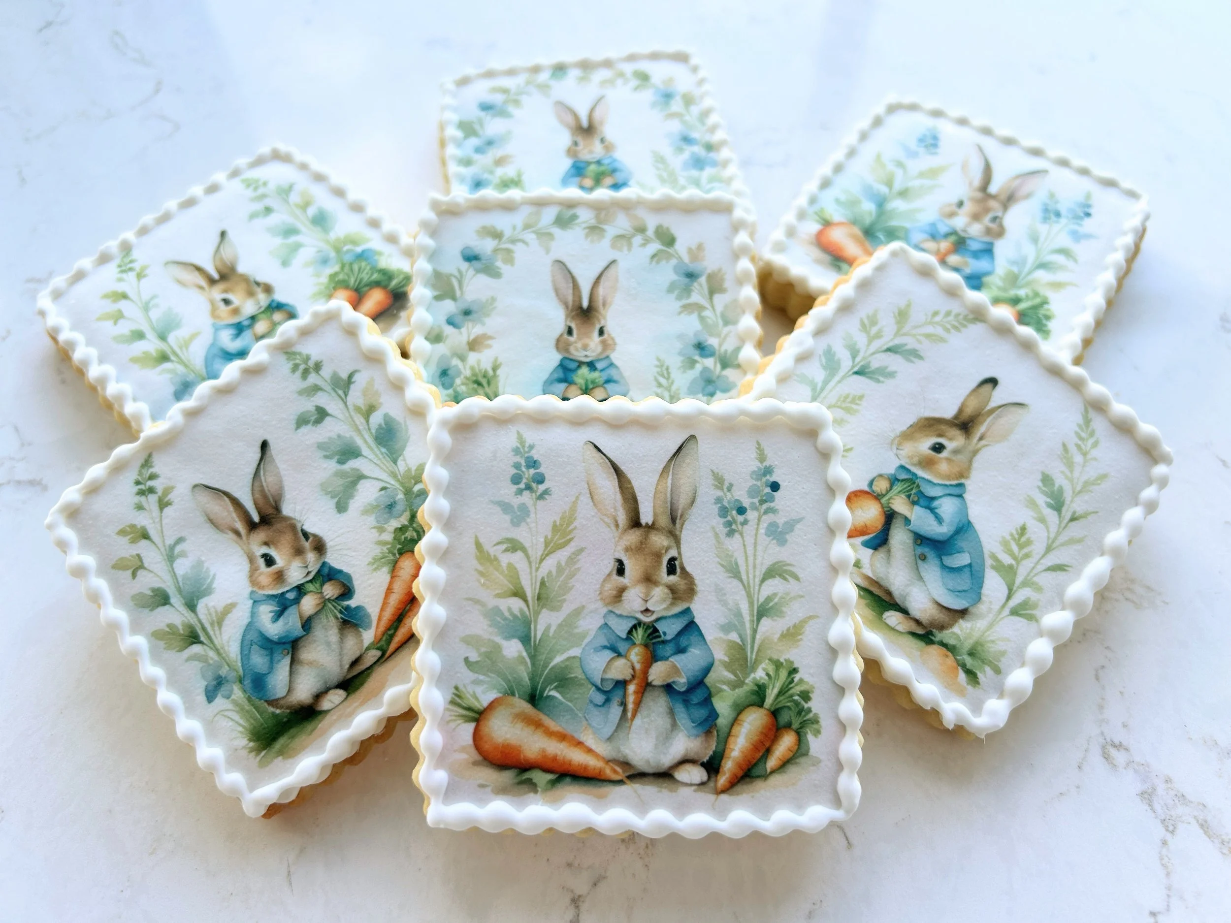 Decorative cookies with bunny illustrations holding carrots, framed with floral patterns and piped white icing borders.