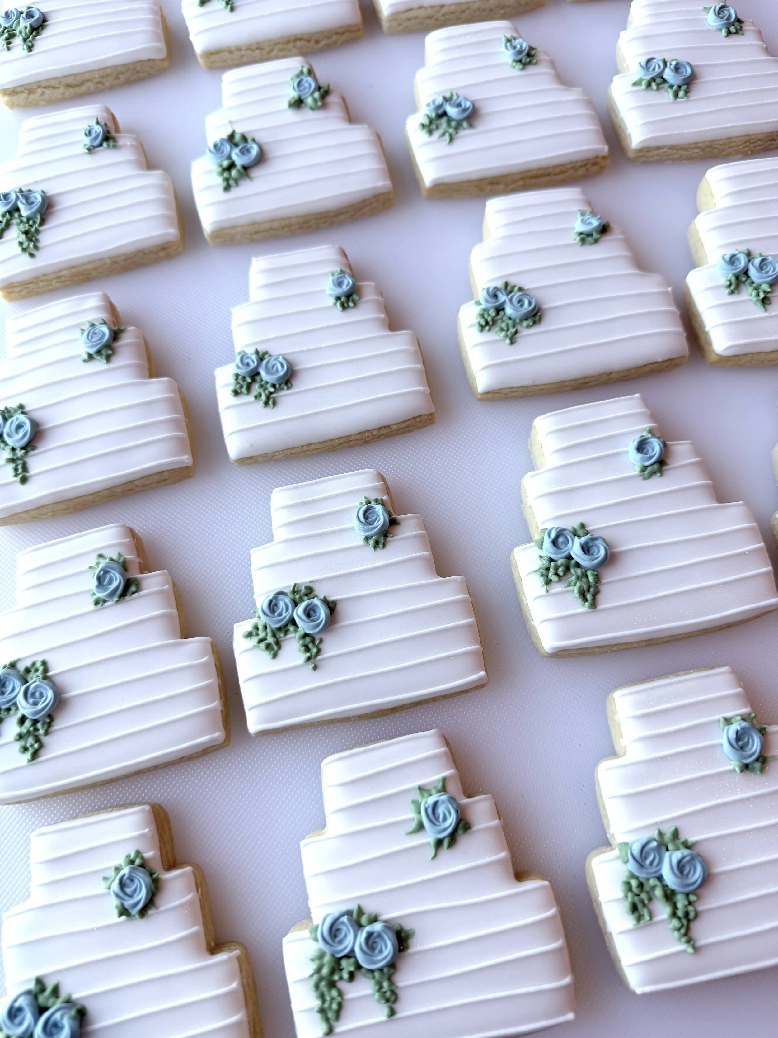 Sugar cookies decorated with white icing and blue rose piping, arranged in a pattern on a white surface.
