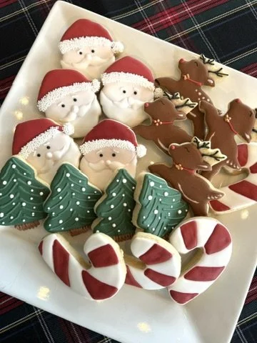 Christmas-themed cookies on a white plate, including Santa faces, reindeer, Christmas trees, and candy canes.