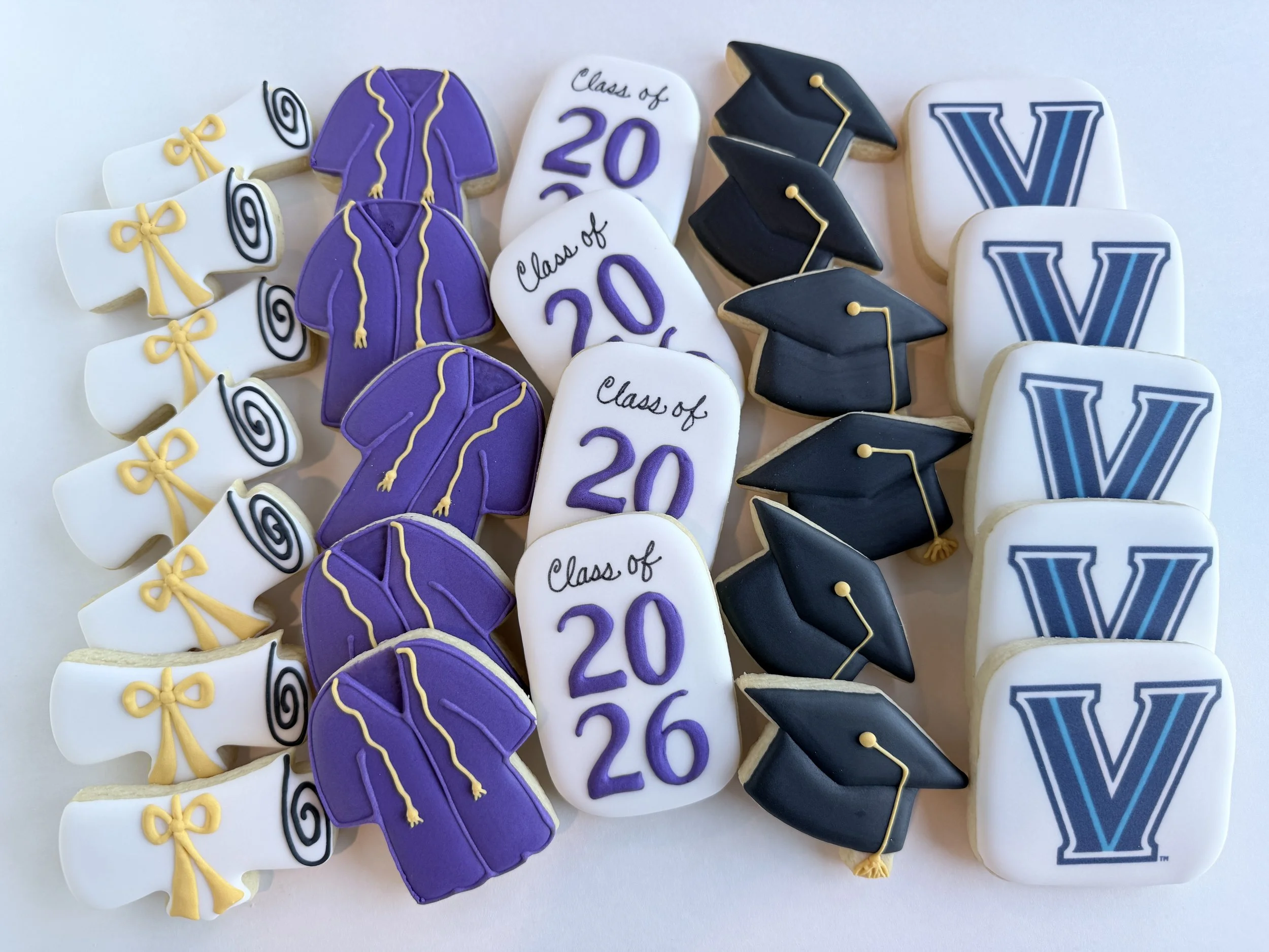 Decorative cookies celebrate a graduation, featuring diplomas, a purple hoodie, mortarboards, and a large letter 'V'.