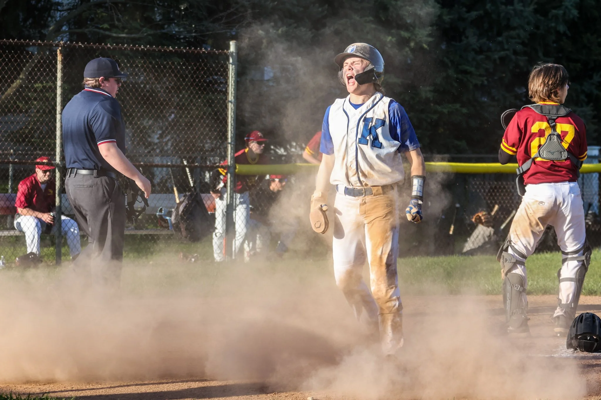 A baseball player celebrating after scoring a run with dust around him, wearing a helmet, gloves, and a sports uniform