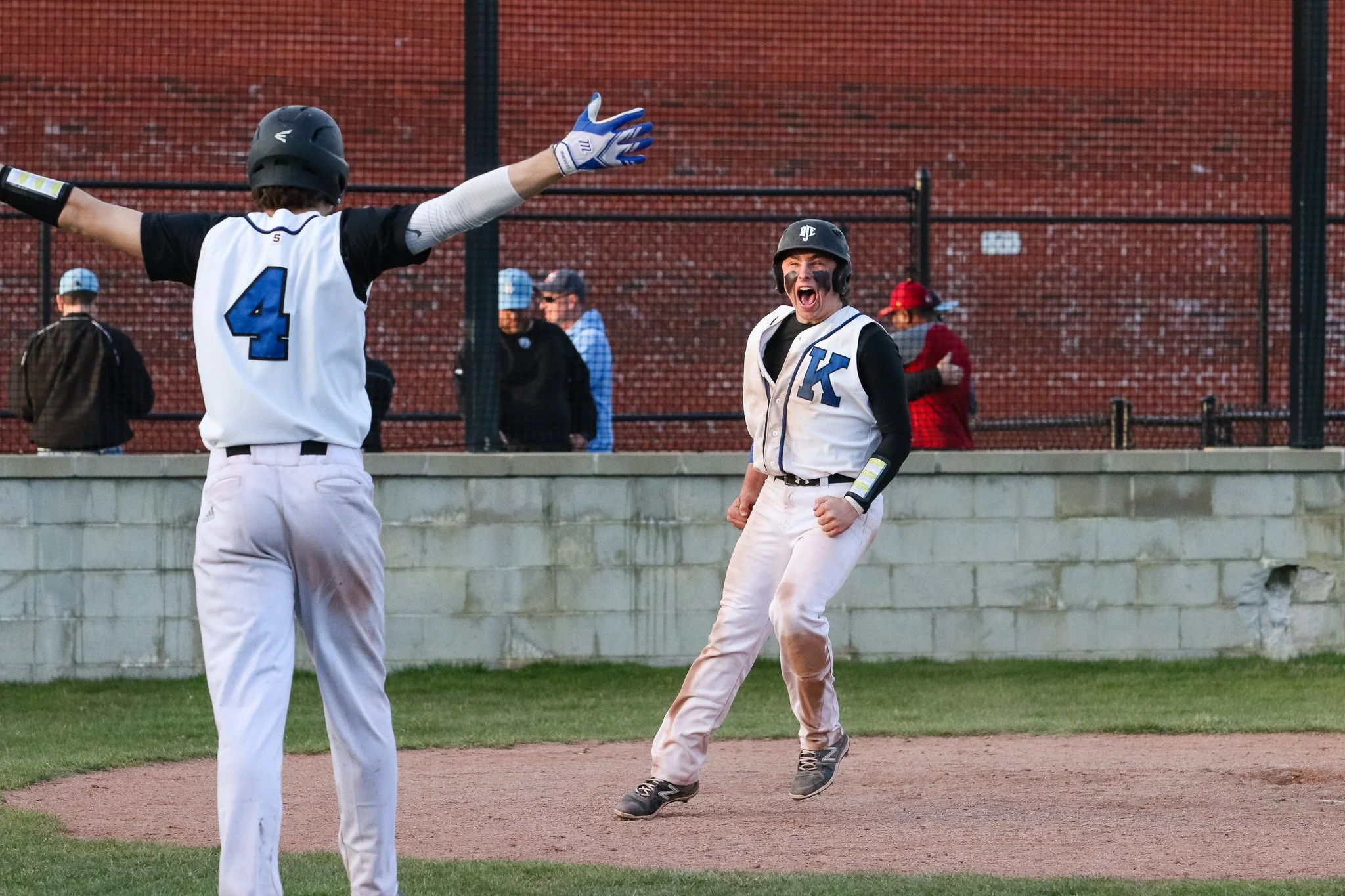Baseball players celebrating on the field, one with arms outstretched and the other jumping for joy, during a game.