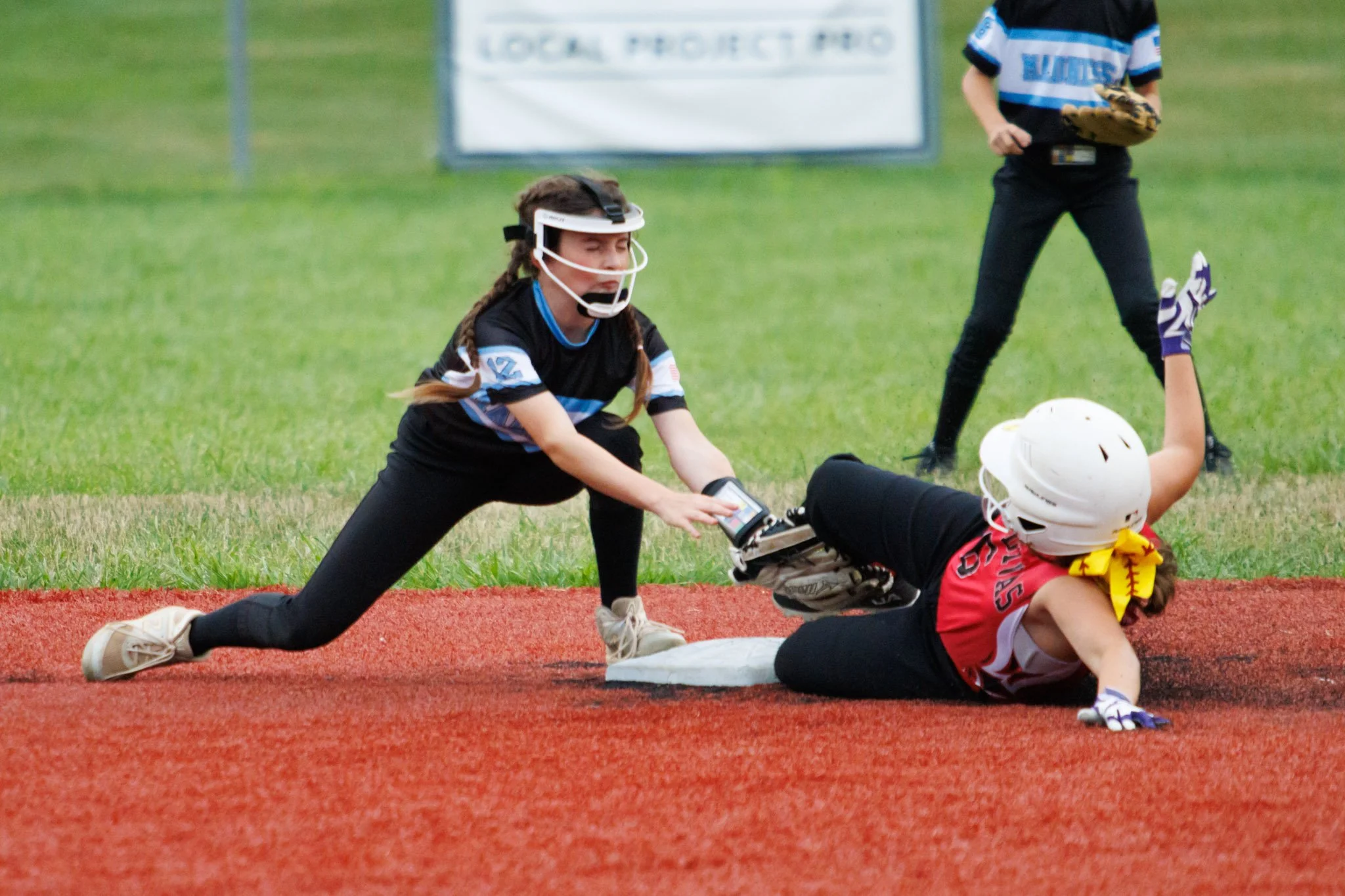 A girl sliding into home plate in a youth softball game, with players in protective gear and an umpire nearby.