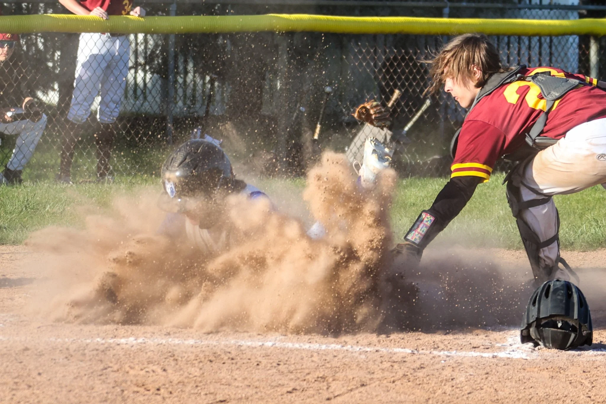 A baseball player sliding into home plate while a catcher attempts to tag him out during a game, with dust flying up from the dirt field.