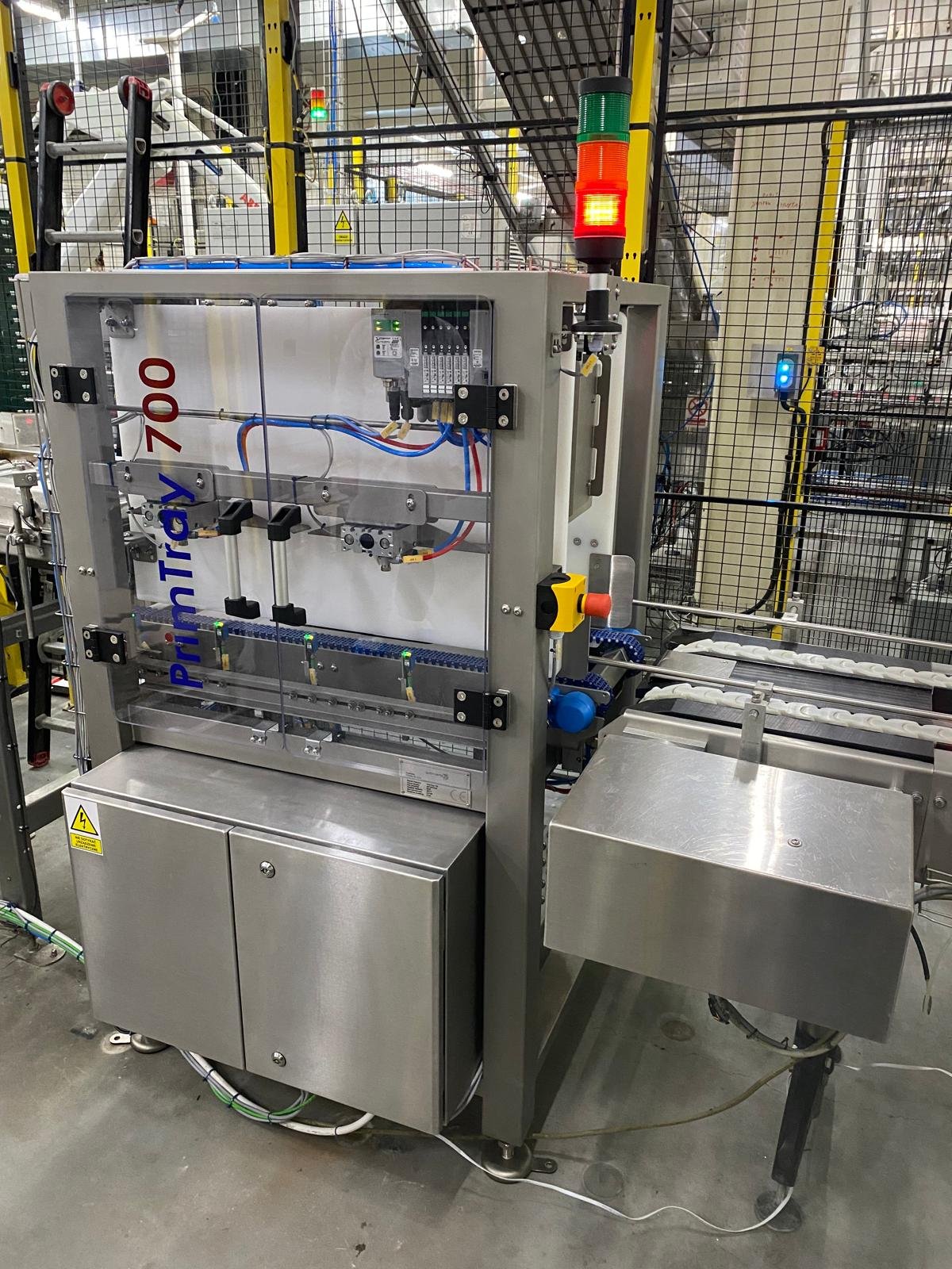 Industrial packaging machine with a red and green warning light on top and a transparent front panel, set up in a factory environment. The machine has the words 'PrintTroy 700' printed on the side.